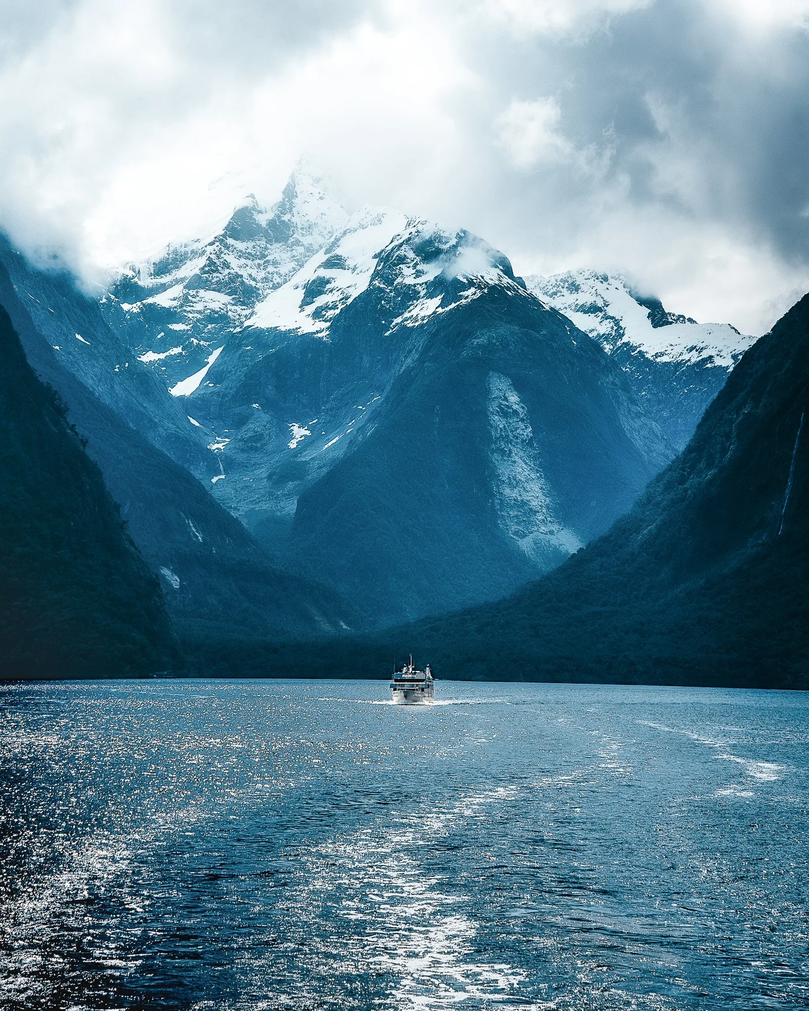 A boat on a lake with snow-capped mountains in the background under a cloudy sky.
