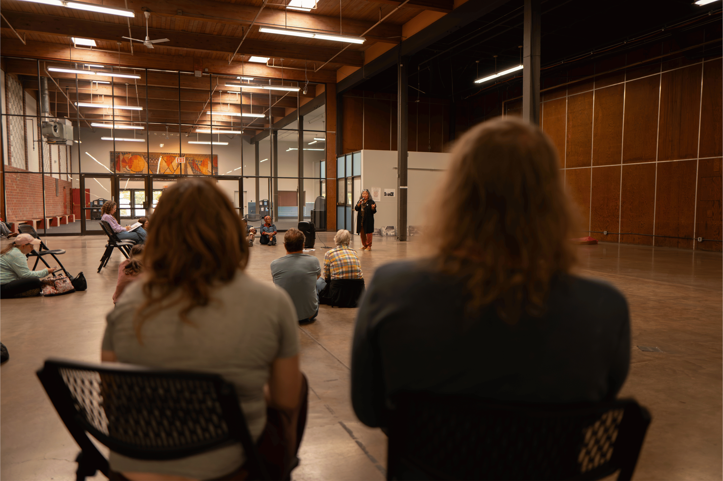  Artist and community organizer Chisao Hata addressing bus tour participants at Portland Expo Center Hall A, a former WWII Japanese American incarceration site, during Kenton Roots on September 12, 2026.  Photo: Troy Winslow / Vanport Mosaic.  