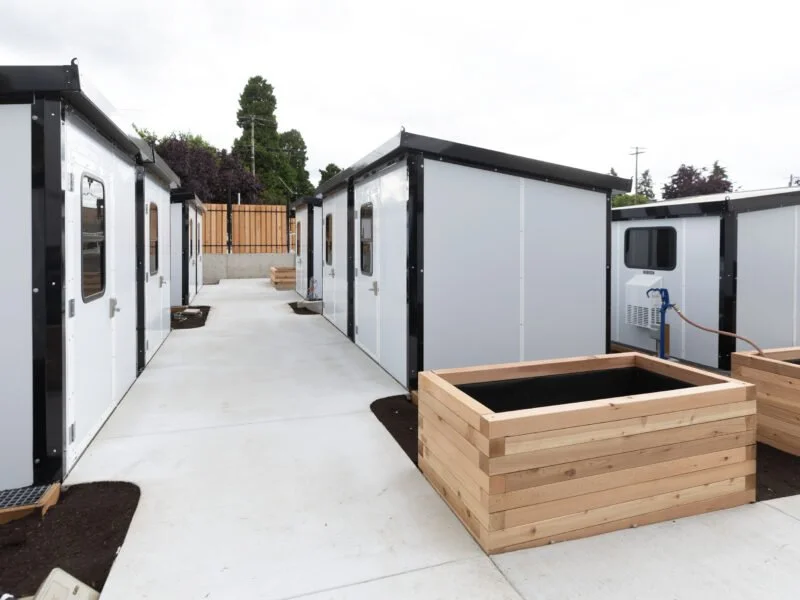 Three, white tiny shelters with wooden planters on either side of the row.