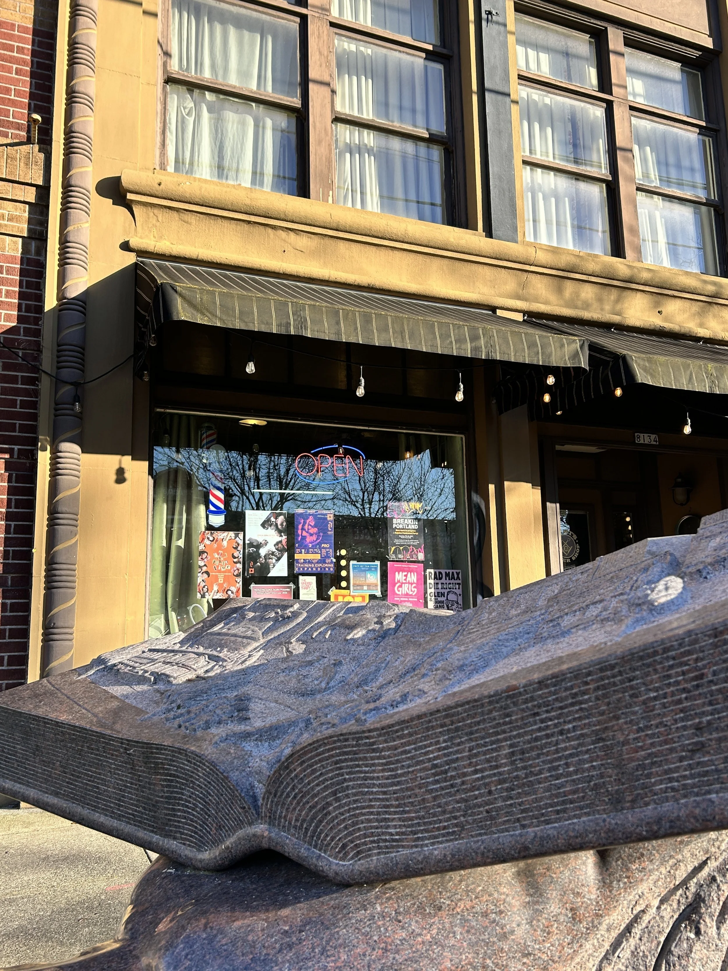 Stone sculpture resembling an open book; in the background, the storefront of a business is visible.