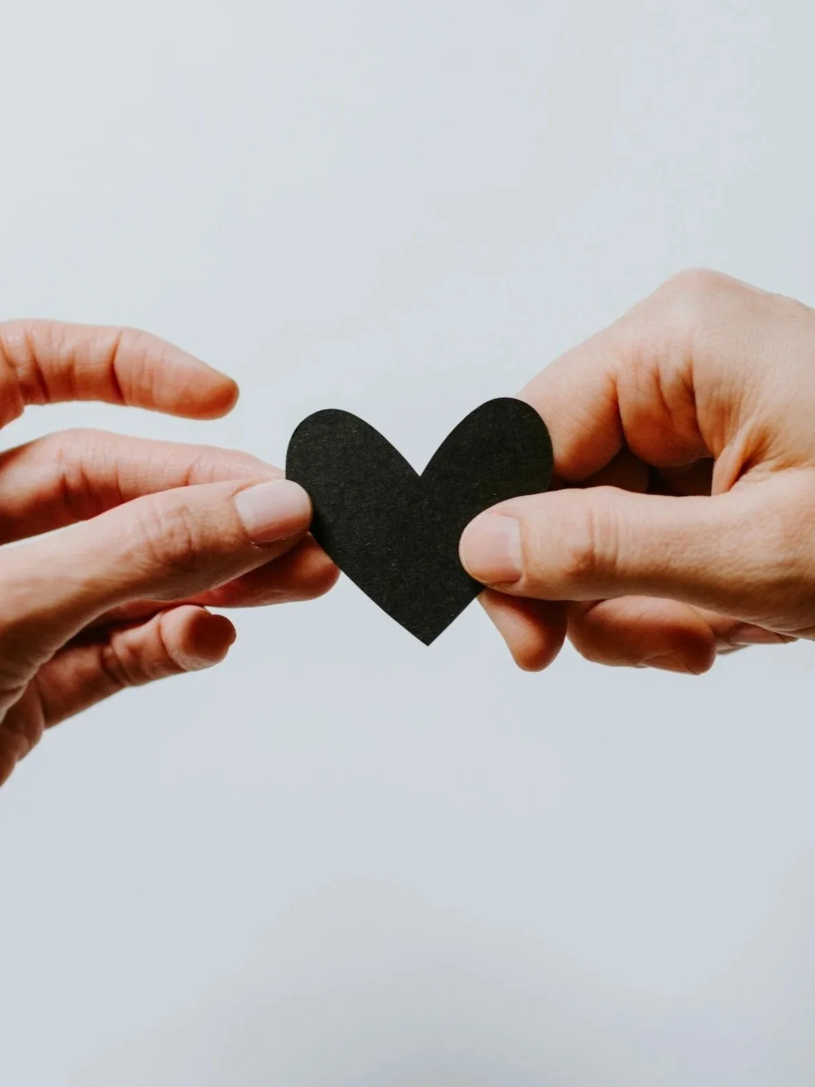 Two hands hold a black heart cutout.