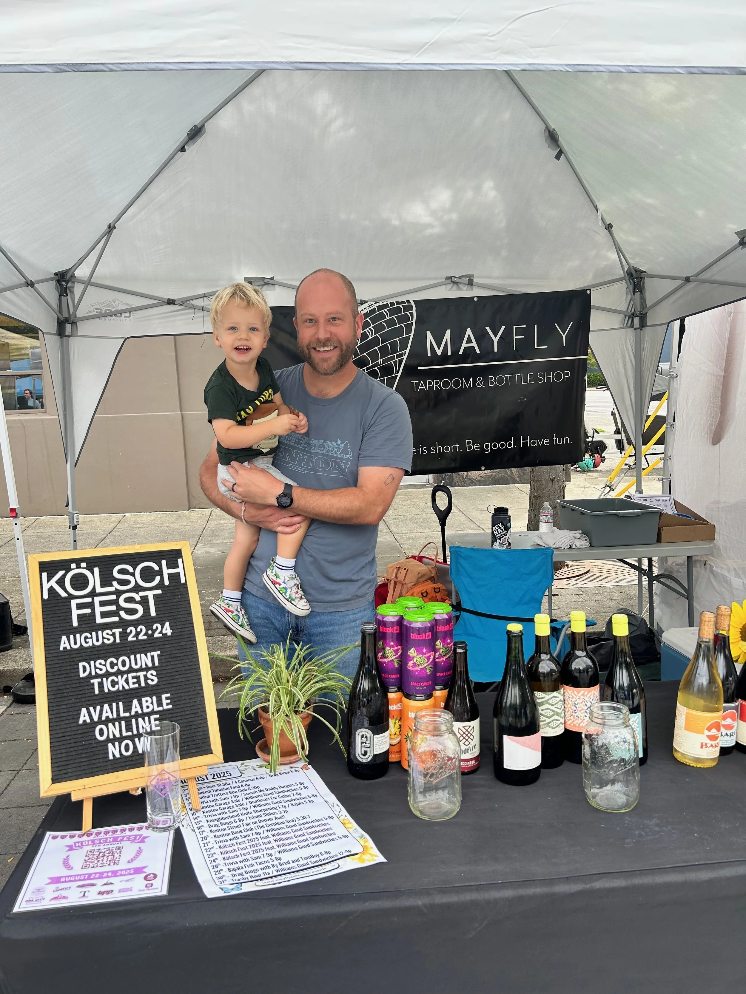 A man holds a child while staffing the Mayfly Taproom booth at the Kenton Street Fair.