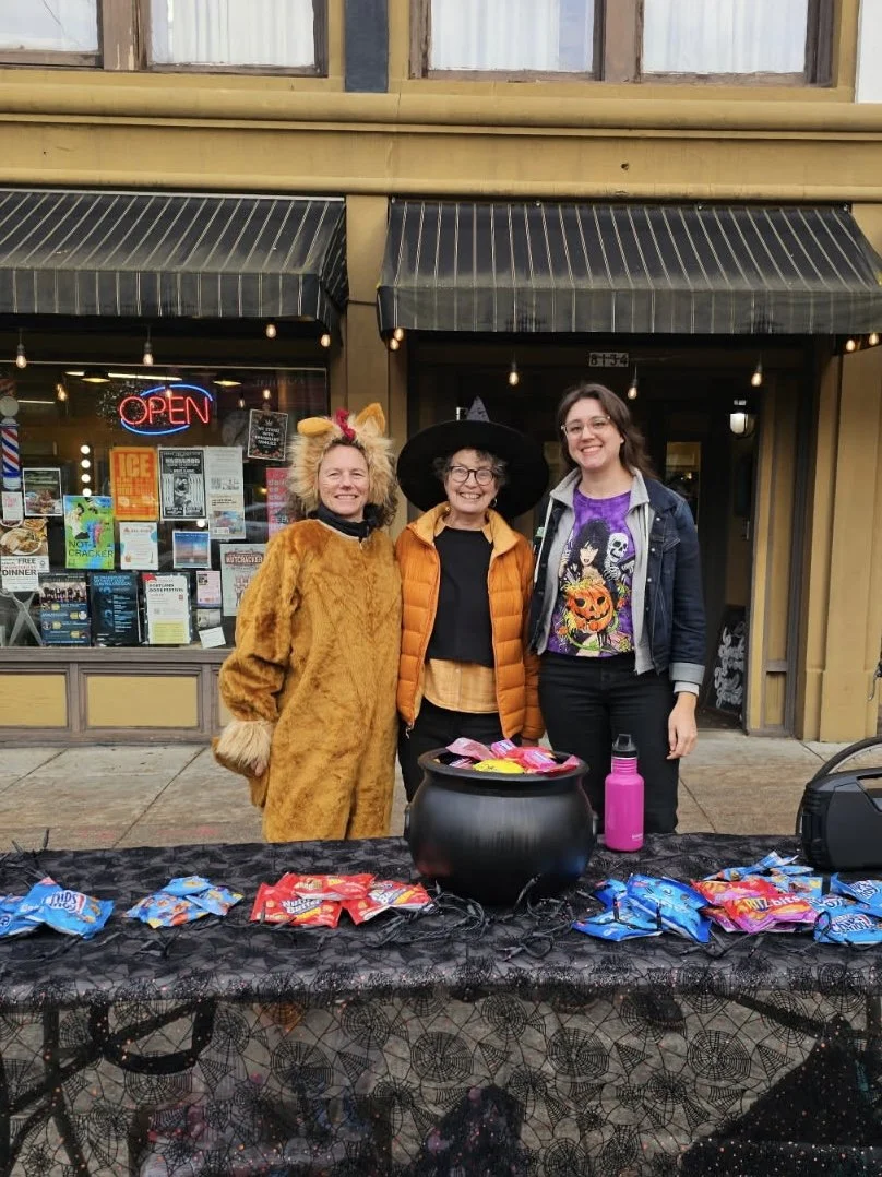 Three women with Halloween-themed outfits smile while posing for a group photo at a neighborhood trick or treat event.