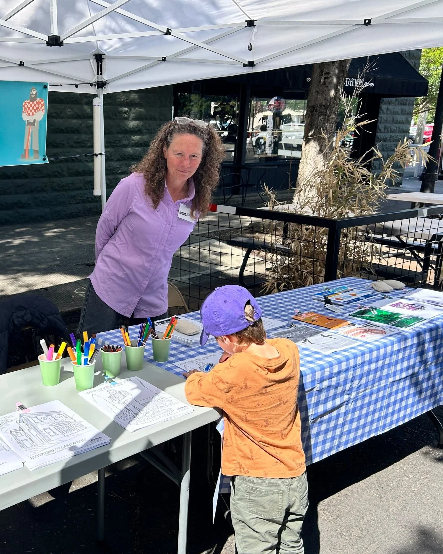 At an outdoor information booth, a child completes a coloring sheet while and adult observes.