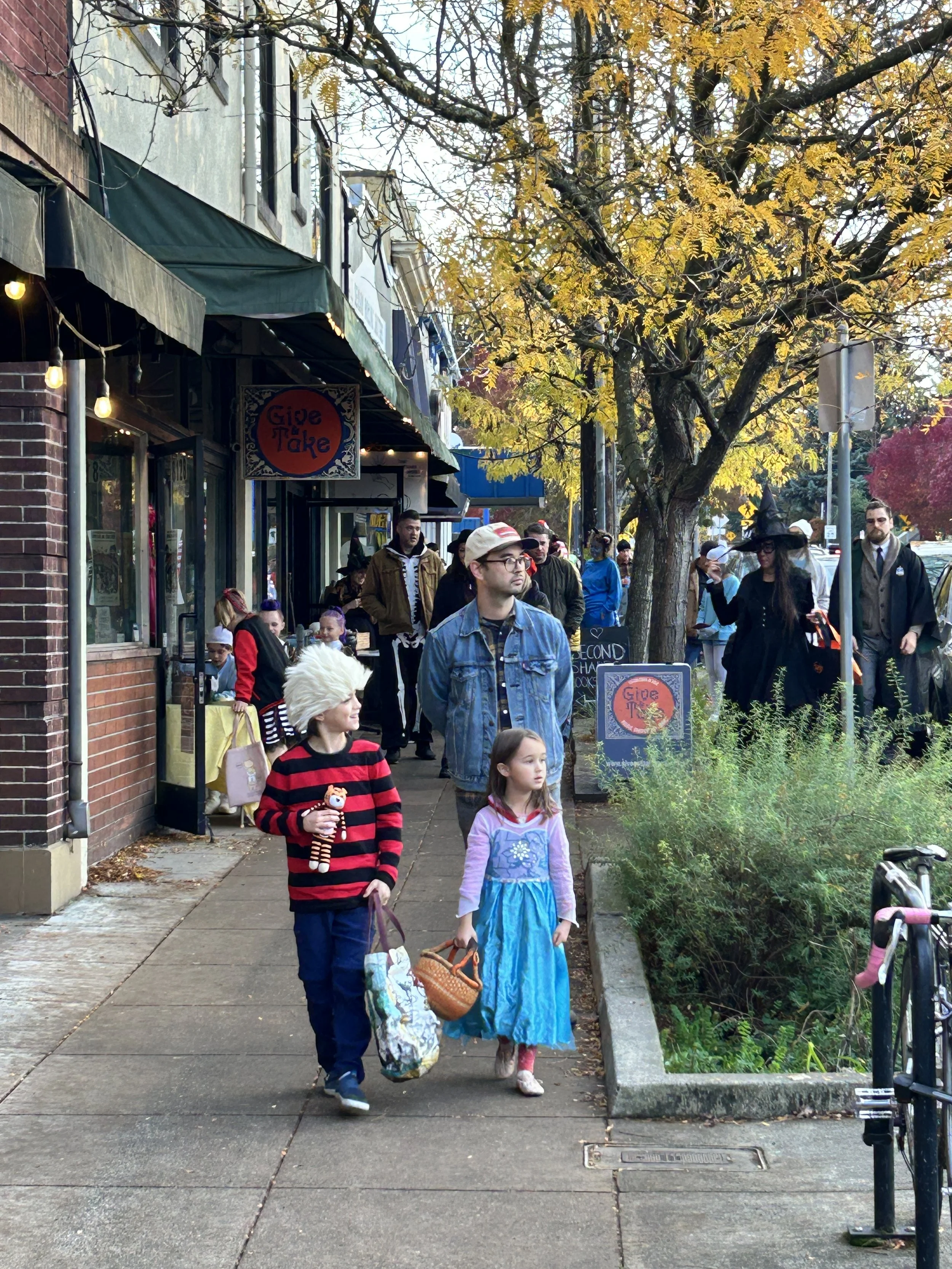 Children and adults dressed in Halloween costumes search for treats offered by local businesses.