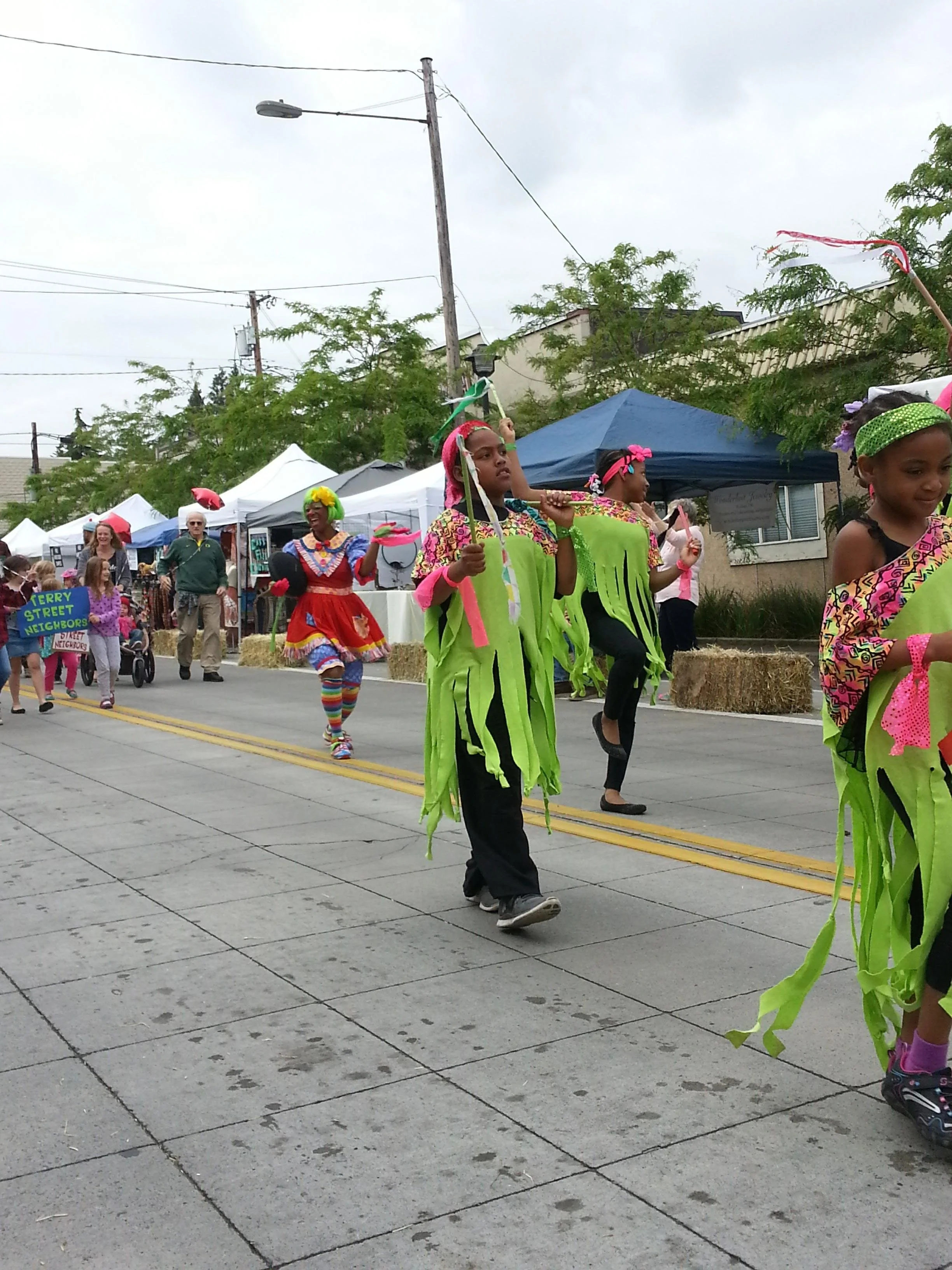 Children dressed in colorful green and pink costumes march in a parade down N Denver