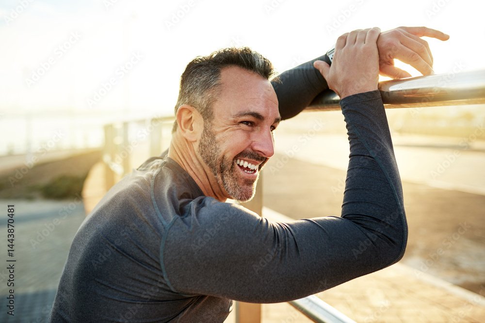Smiling man leaning on a railing outdoors at sunset, wearing athletic clothing.