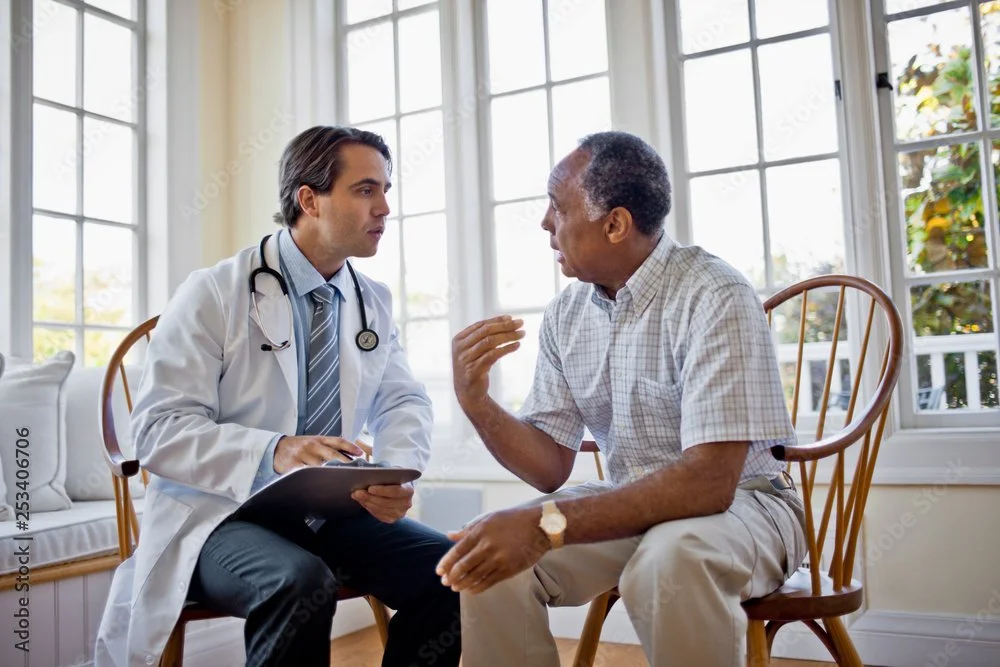 Doctor and elderly patient having a discussion in a well-lit room with large windows.