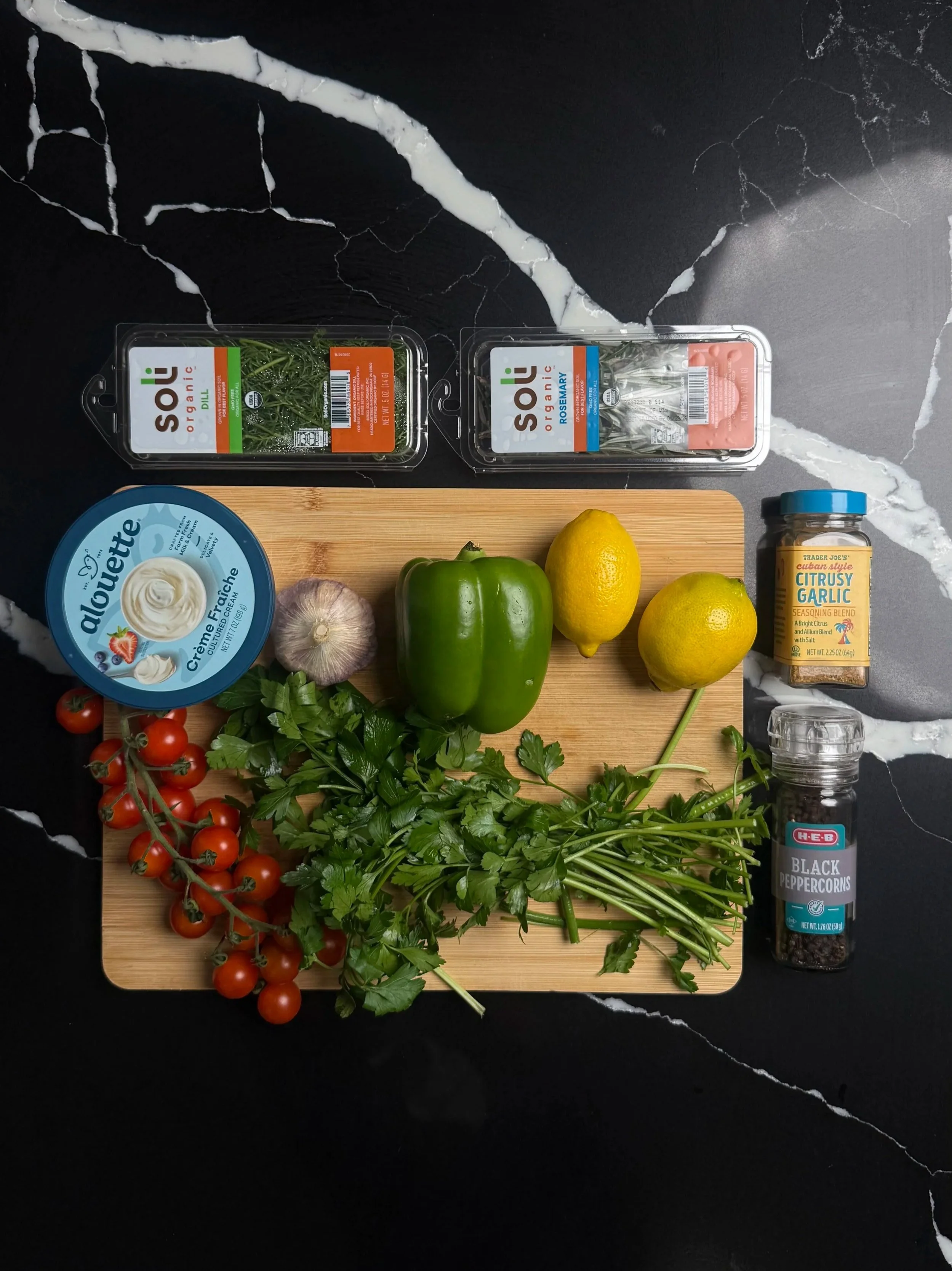 Ingredients for pan-seared trout including fresh trout fillets, parsley, crème fraîche, cherry tomatoes, lemon, garlic, and rosemary