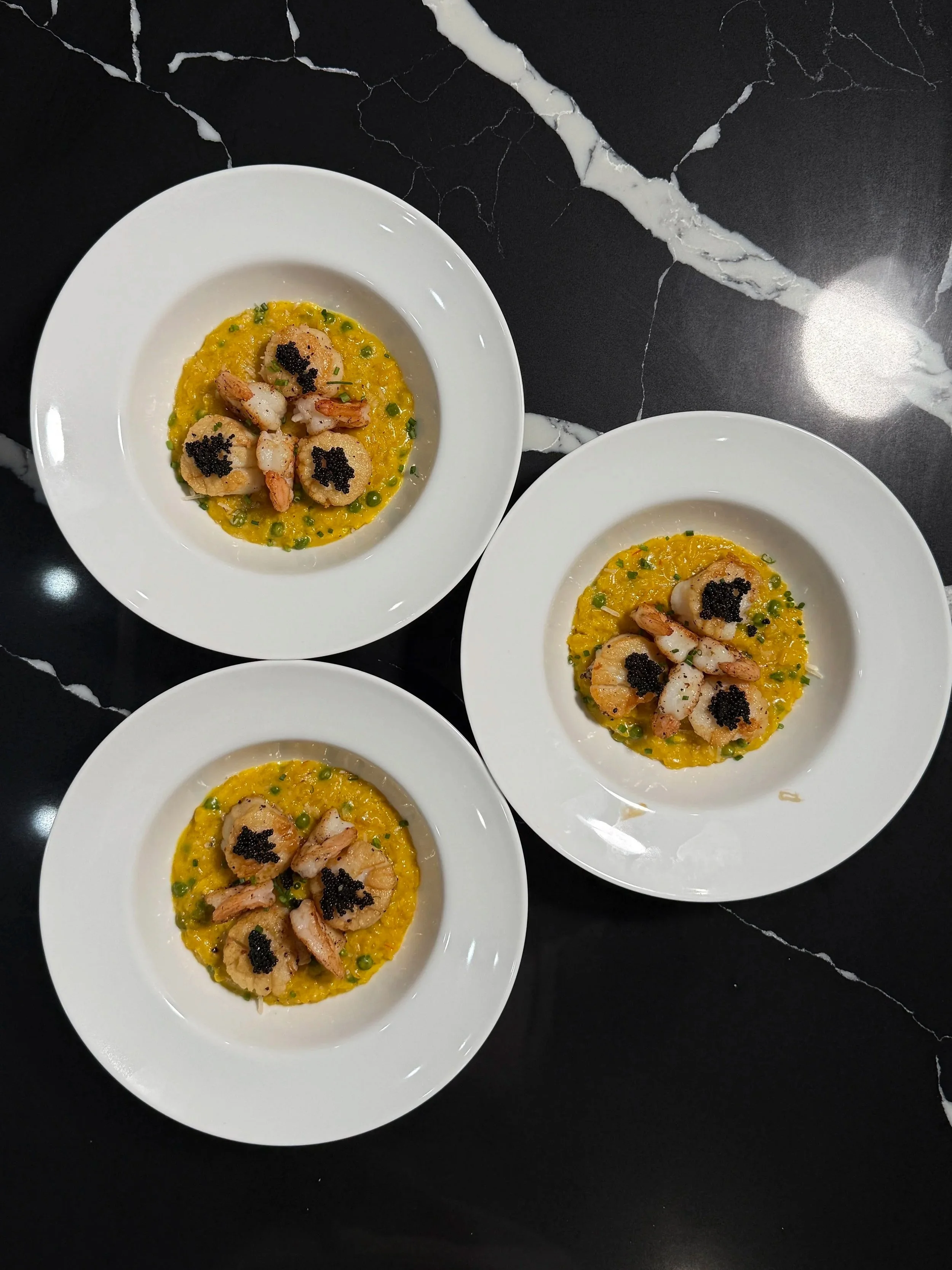 Finished saffron seafood risotto with scallops, shrimp, peas and caviar served in a white bowl.