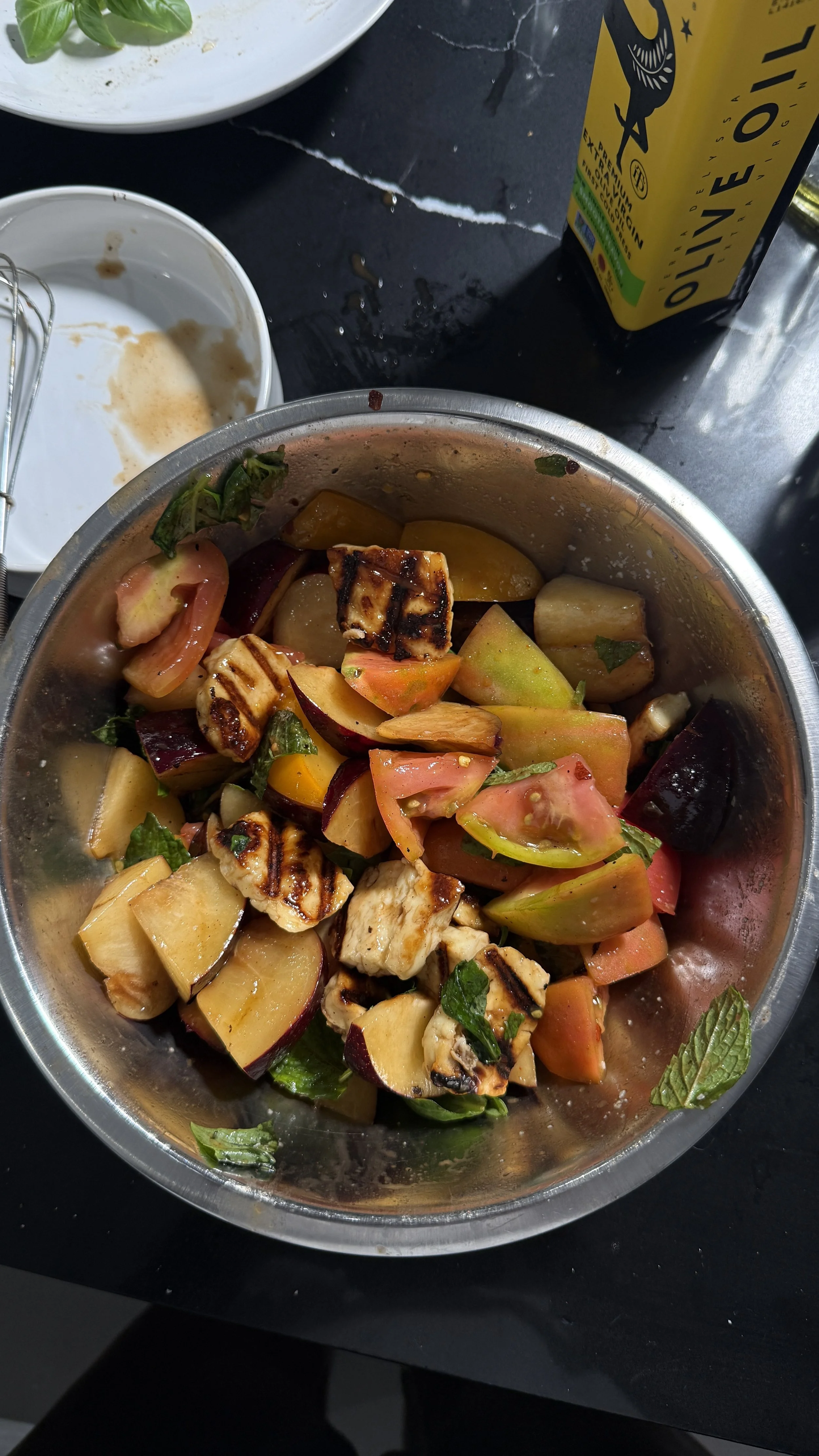 Caprese salad being assembled with plums, tomatoes, halloumi, and herbs