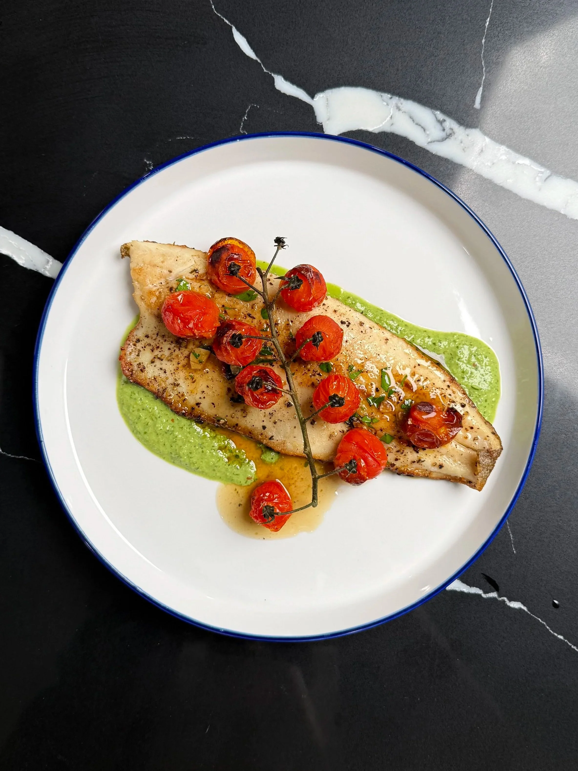 Pan-seared trout with crispy skin served over parsley crème fraîche purée, topped with blistered tomatoes and lemon pan sauce