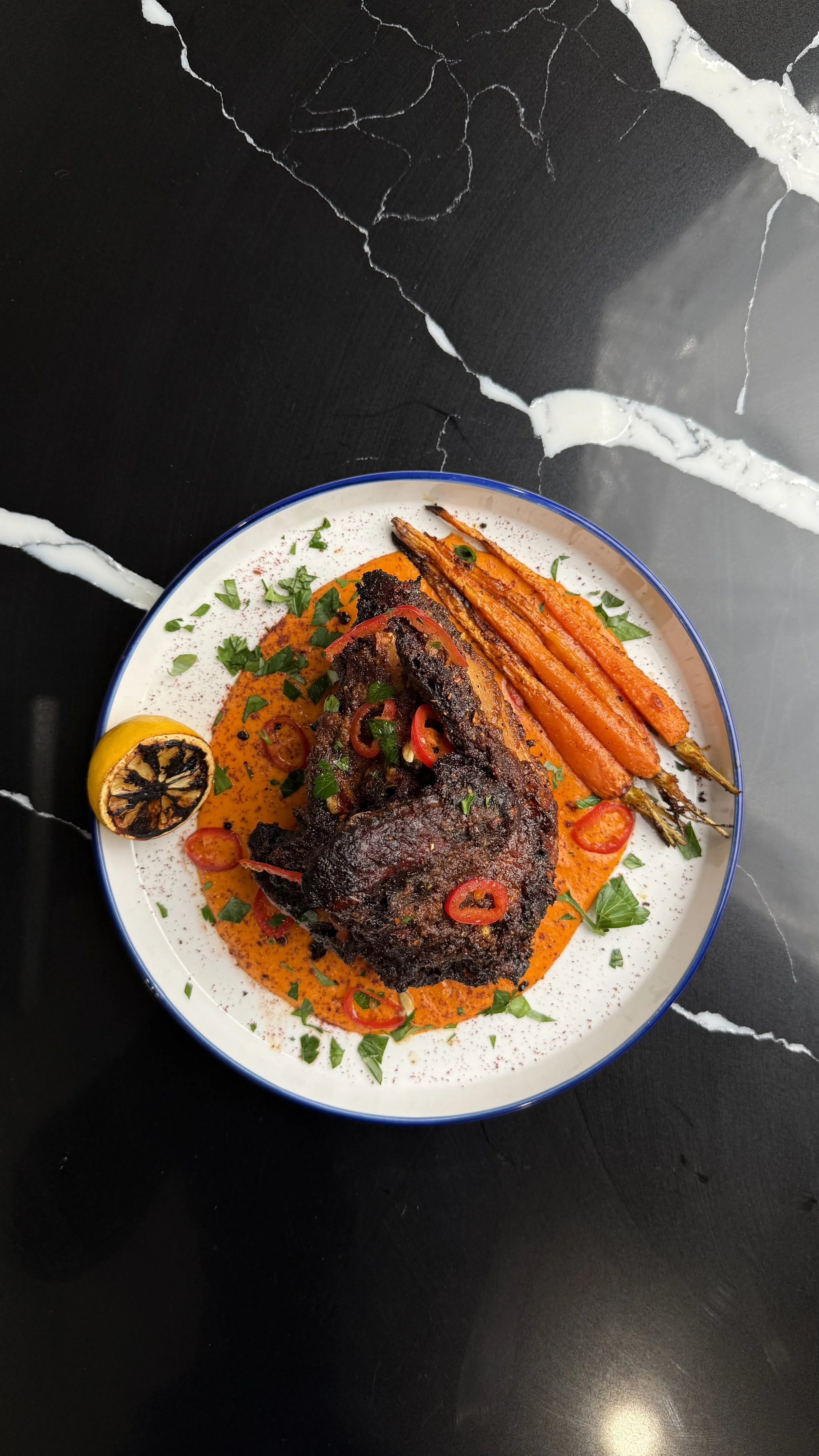 Crispy air fryer half roasted chicken served over mojo rojo with charred paprika carrots, parsley, chili, sumac, and lemon.