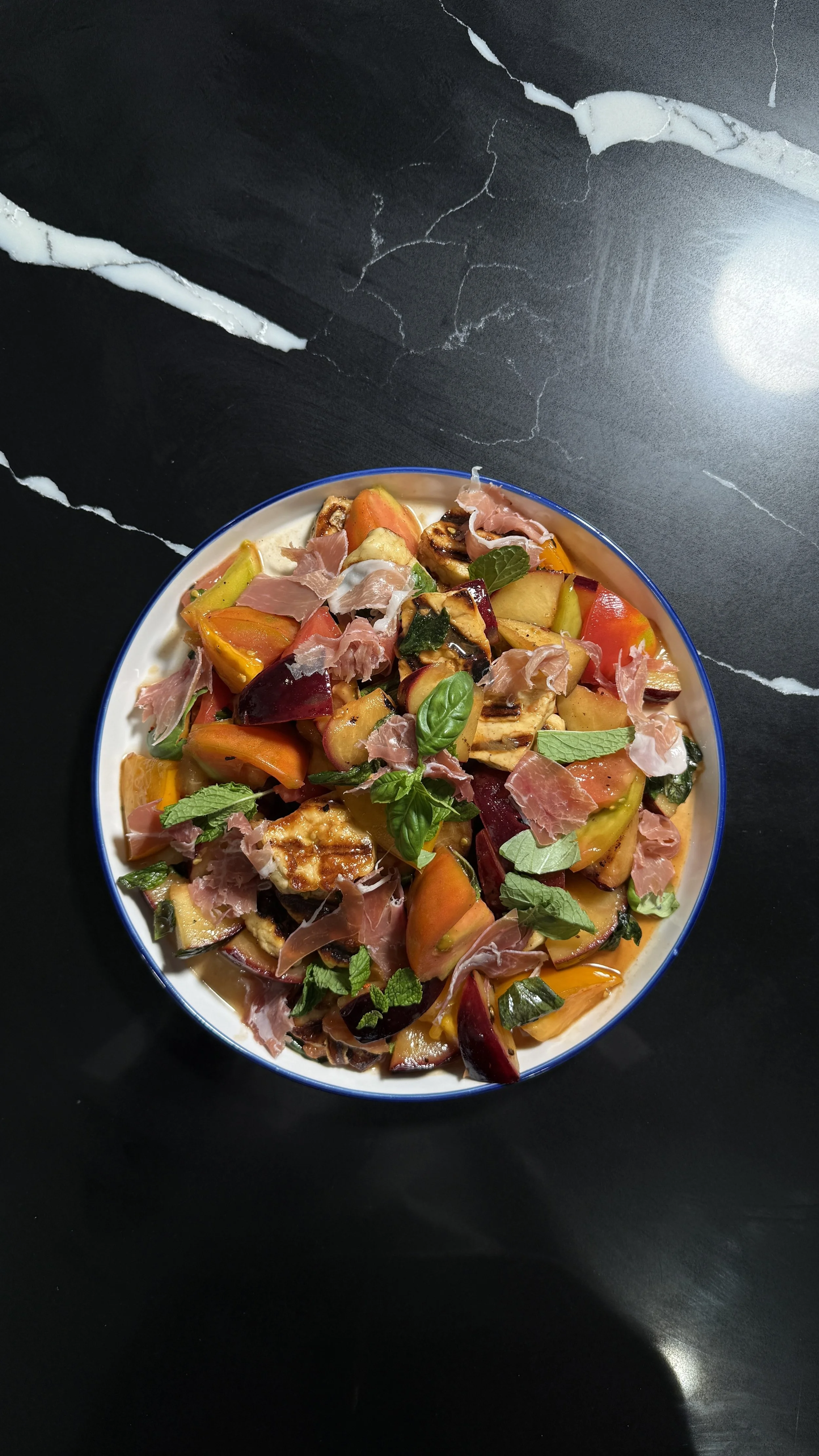 Overhead view of plum and heirloom tomato caprese with prosciutto and herbs