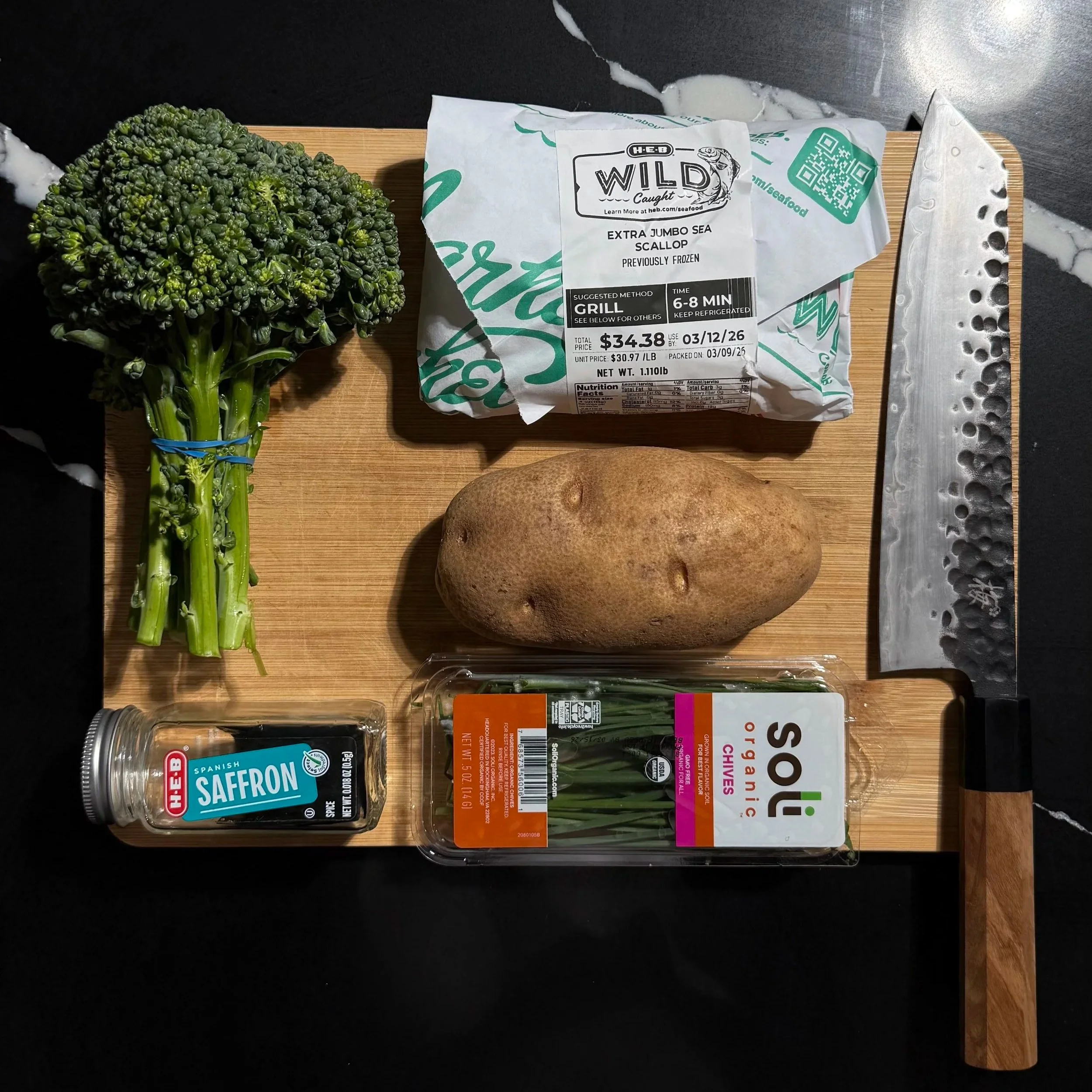 Fresh sea scallops, broccolini, russet potato, saffron threads, and chives arranged on a cutting board for a scallops with saffron beurre blanc recipe.