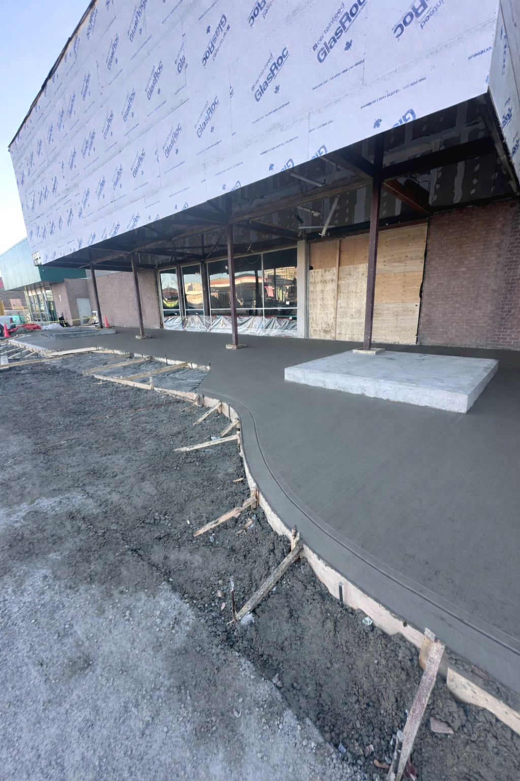 Under construction storefront with new concrete sidewalk and wooden support beams outside a building