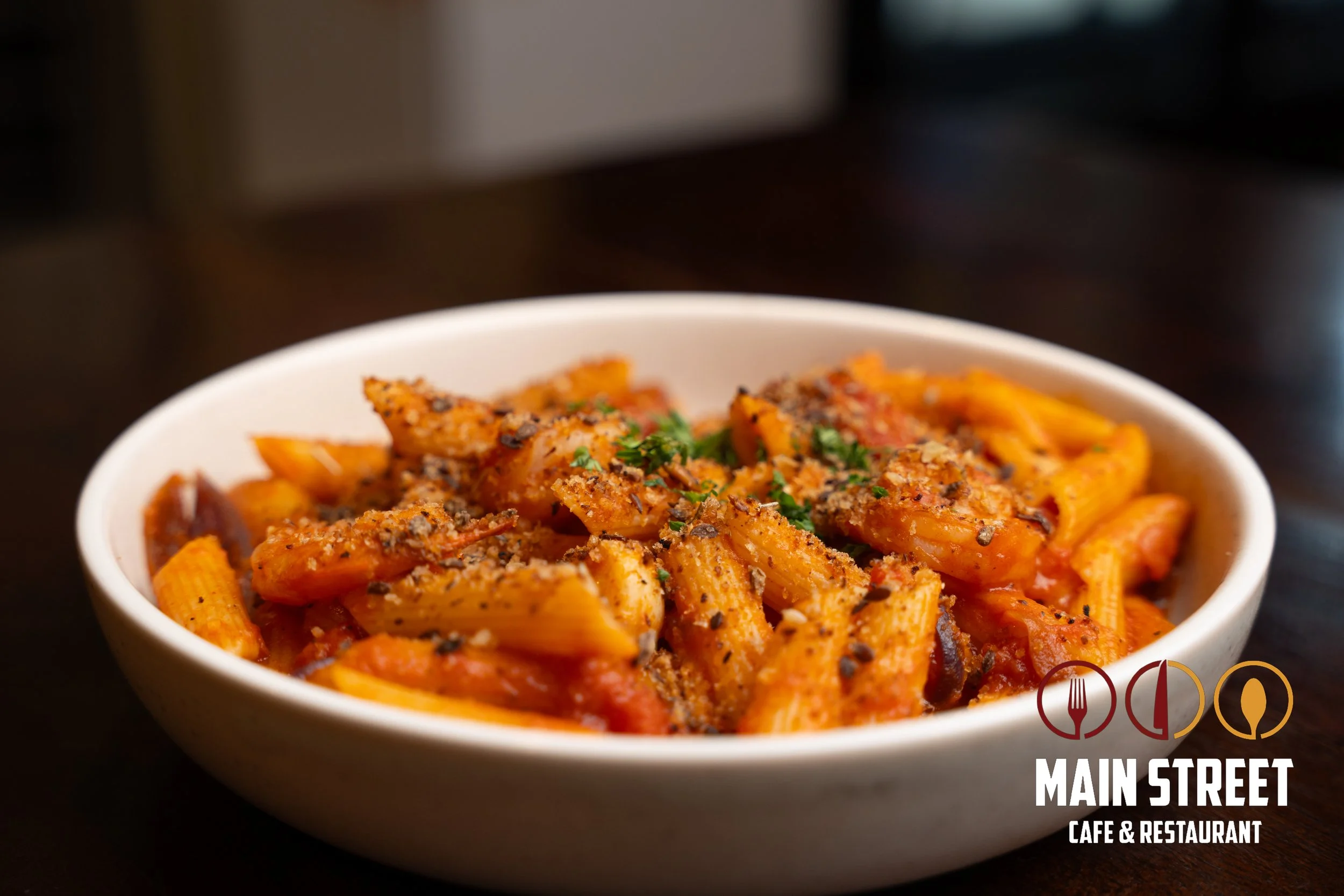 A bowl of pasta with tomato sauce, garnished with chopped herbs and grated cheese, on a dark wooden table.