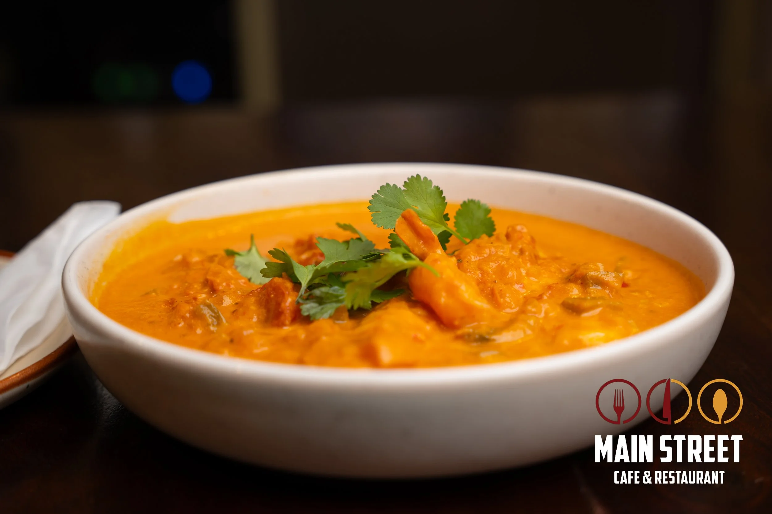 A bowl of orange curry garnished with cilantro leaves at Main Street Cafe & Restaurant.
