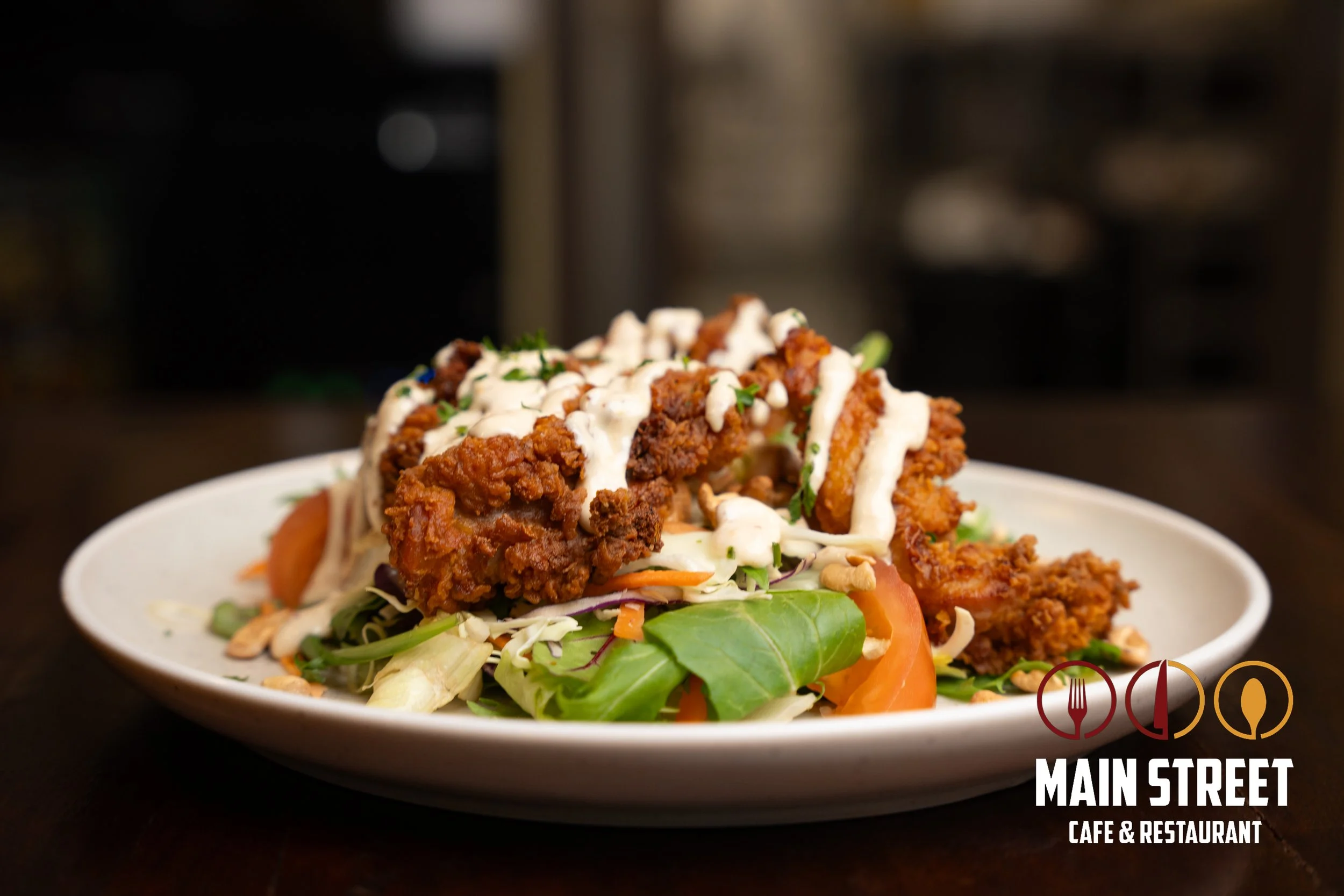 A plate of fried chicken topped with dressing and garnished with herbs, served over a bed of salad with tomatoes and greens, at Main Street Cafe & Restaurant.