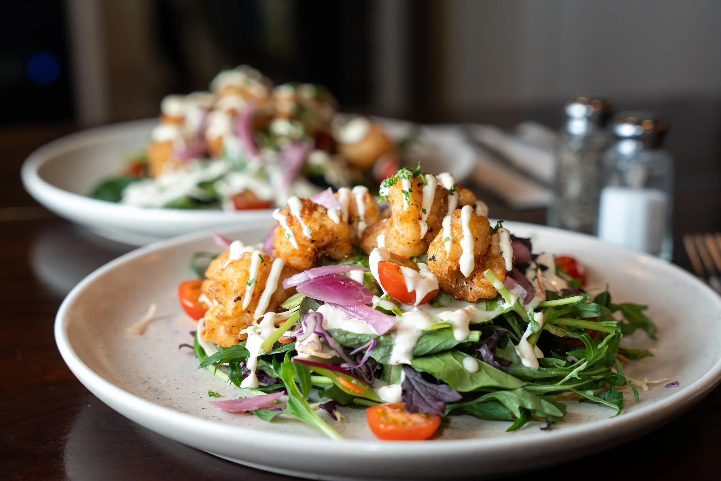 A plate of salad topped with fried chicken pieces, cherry tomatoes, and drizzled with dressing.