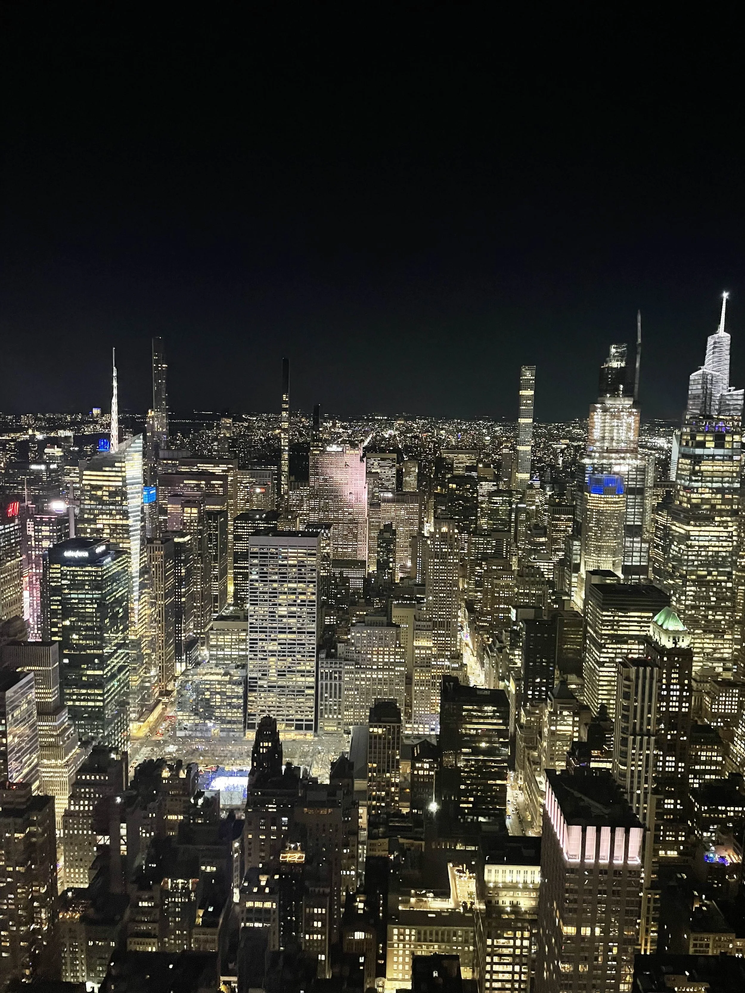 New York City skyline, Nighttime aerial view of a city with illuminated skyscrapers and streets, prominent tall buildings, and a dark sky.