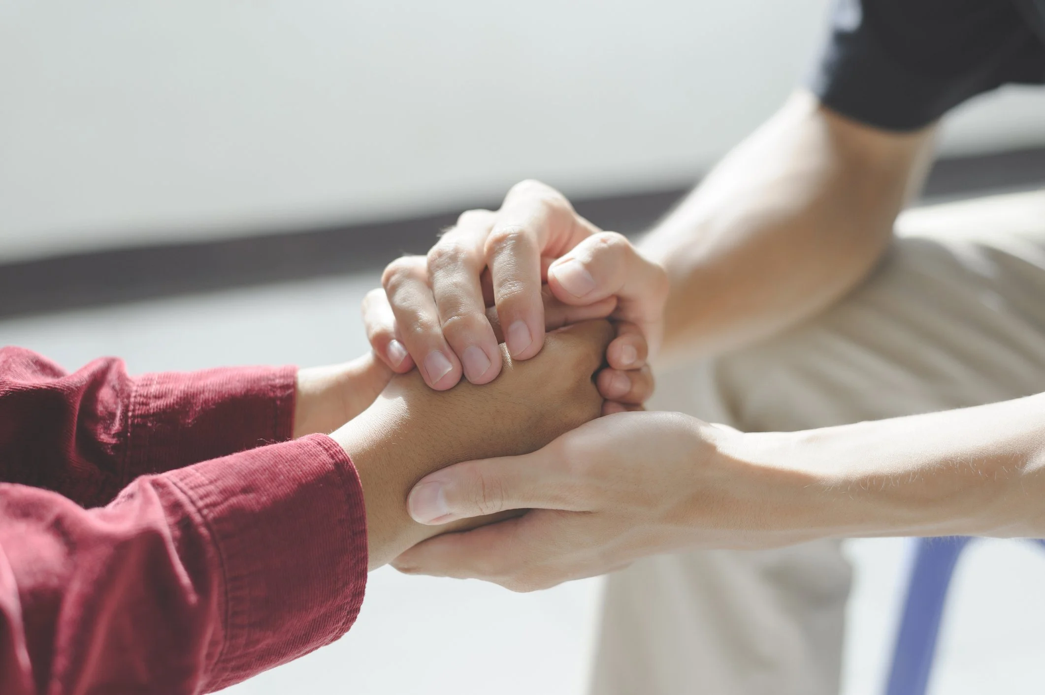 People holding hands in a supportive gesture, one person's hand resting on top of another's.