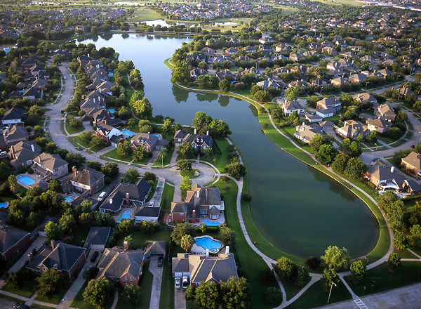 Aerial view of a suburban neighborhood with houses, ponds, and green spaces.
