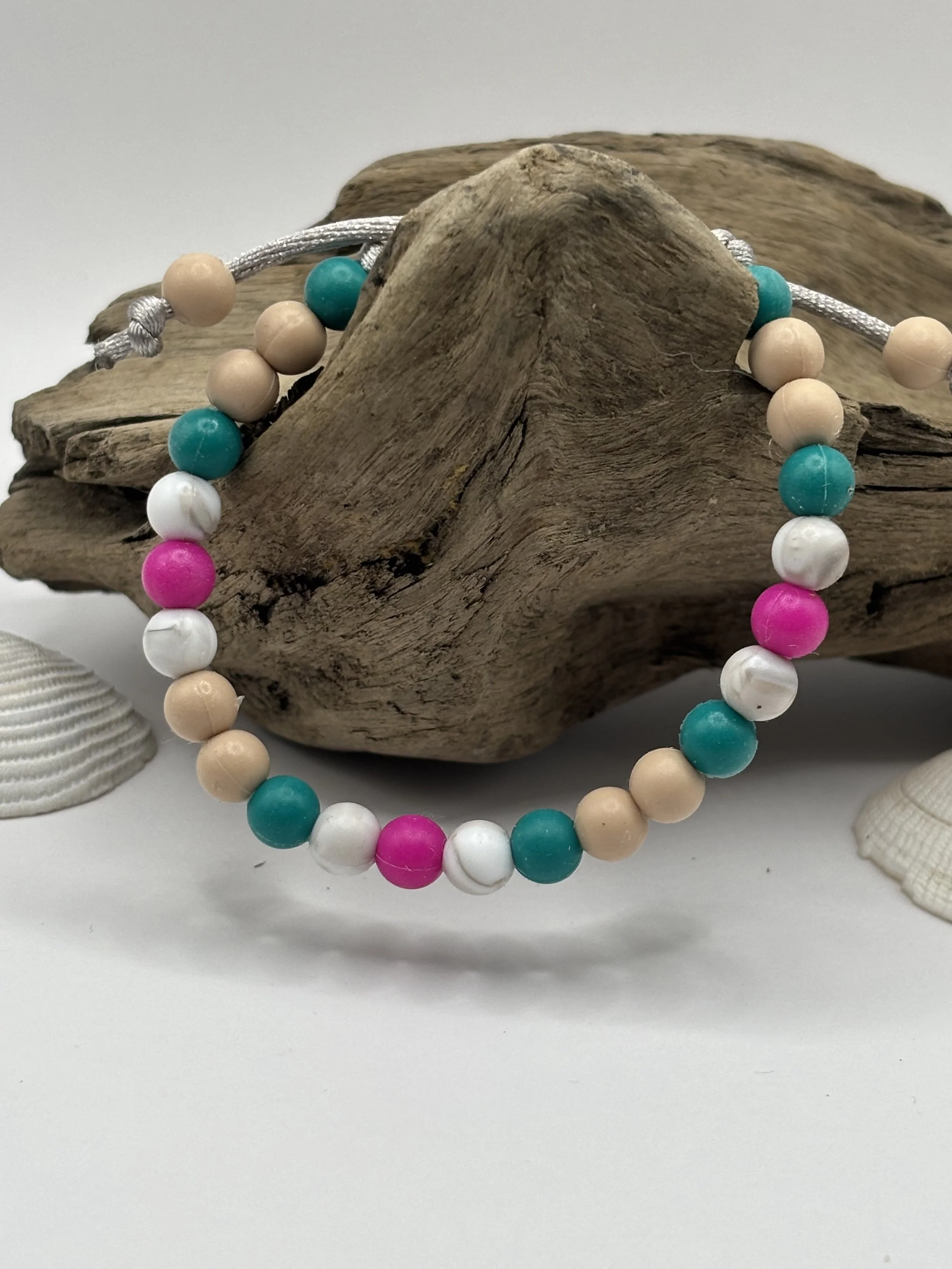 Beaded necklace with colorful beads draped over a piece of driftwood, with shells in the background.