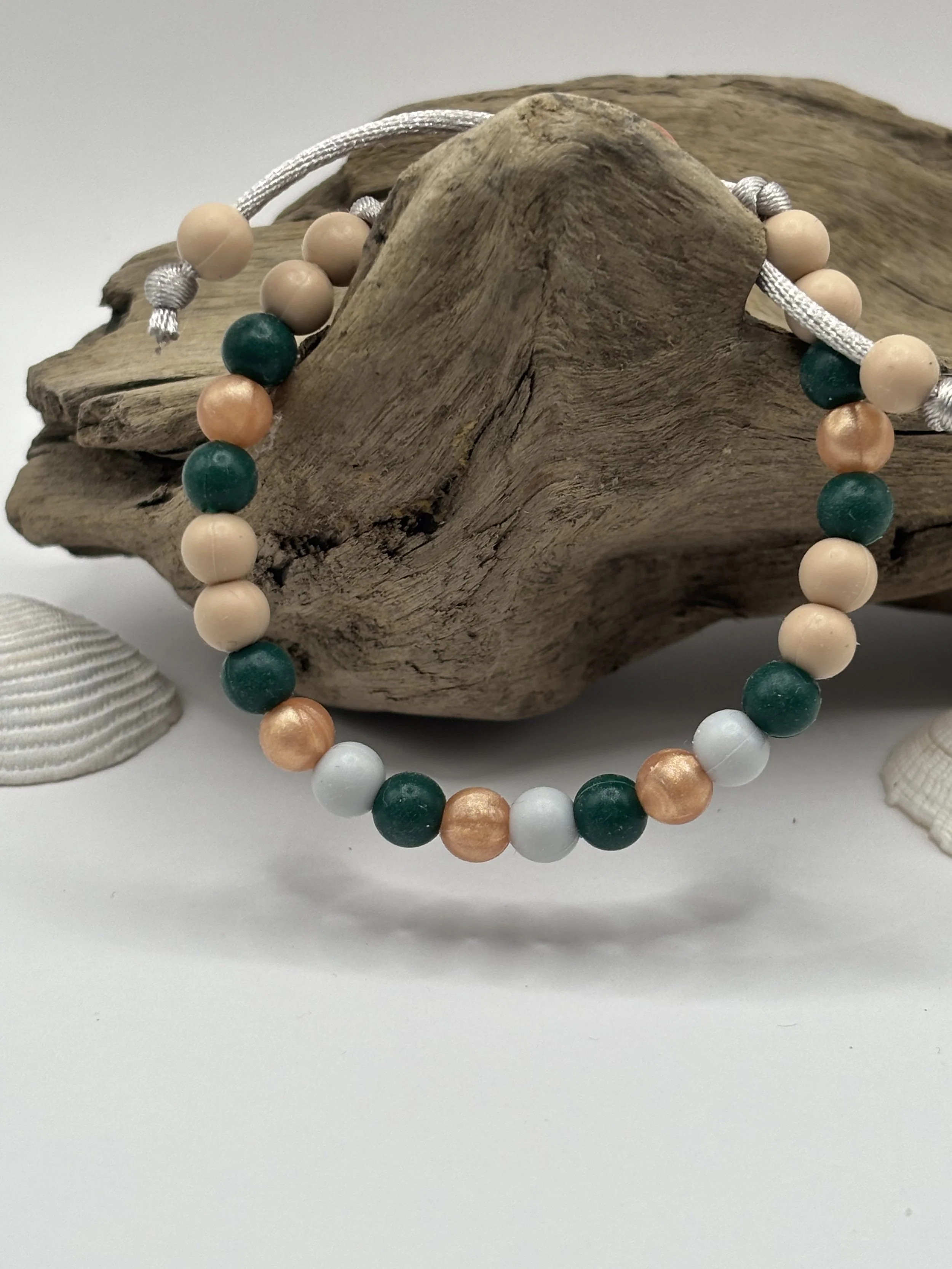 Beaded necklace with cream, teal, white, and copper-colored beads resting on a piece of driftwood with seashells nearby.