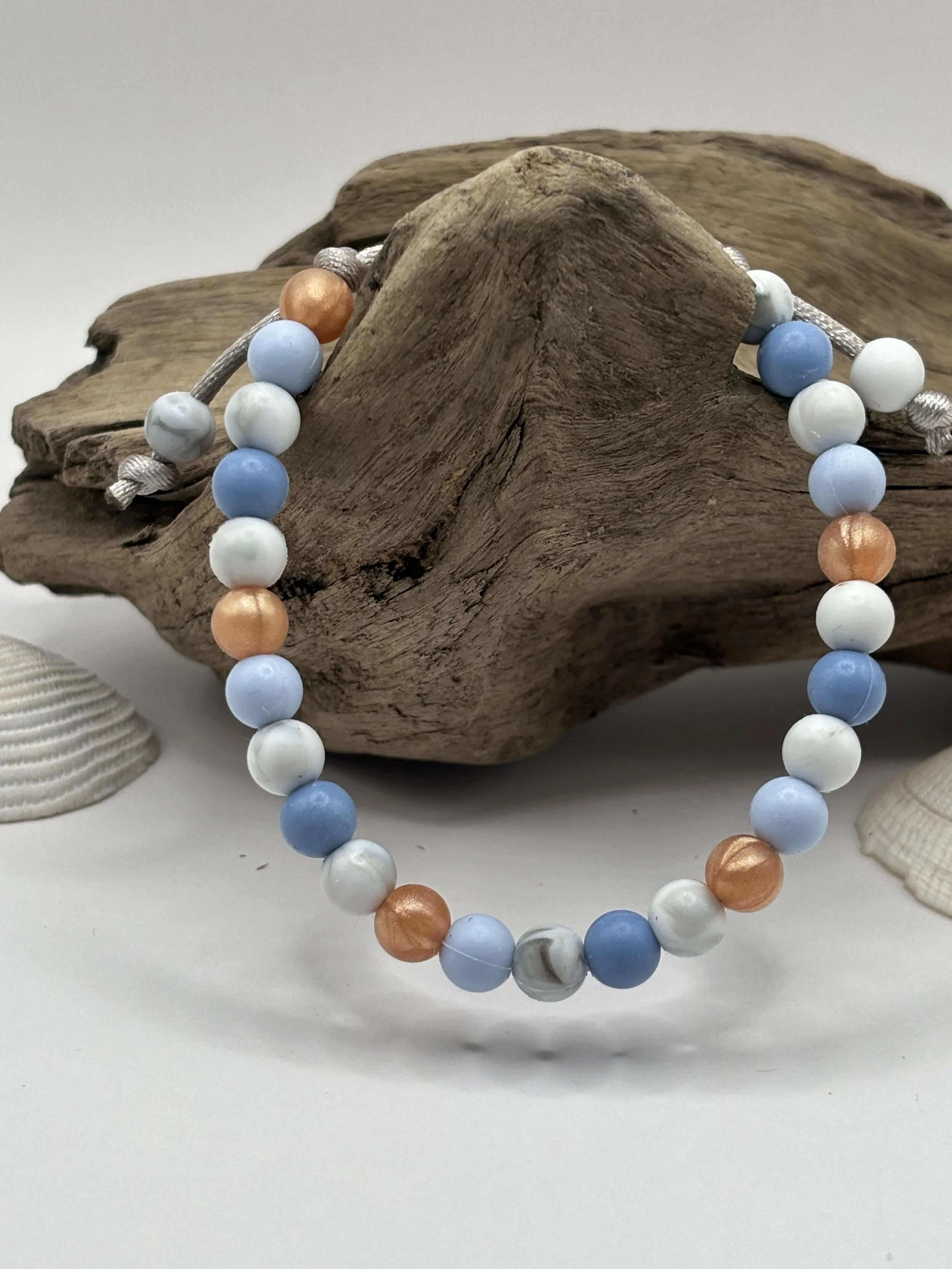Colorful beaded bracelet draped over a piece of driftwood, with seashells nearby, on a white background.