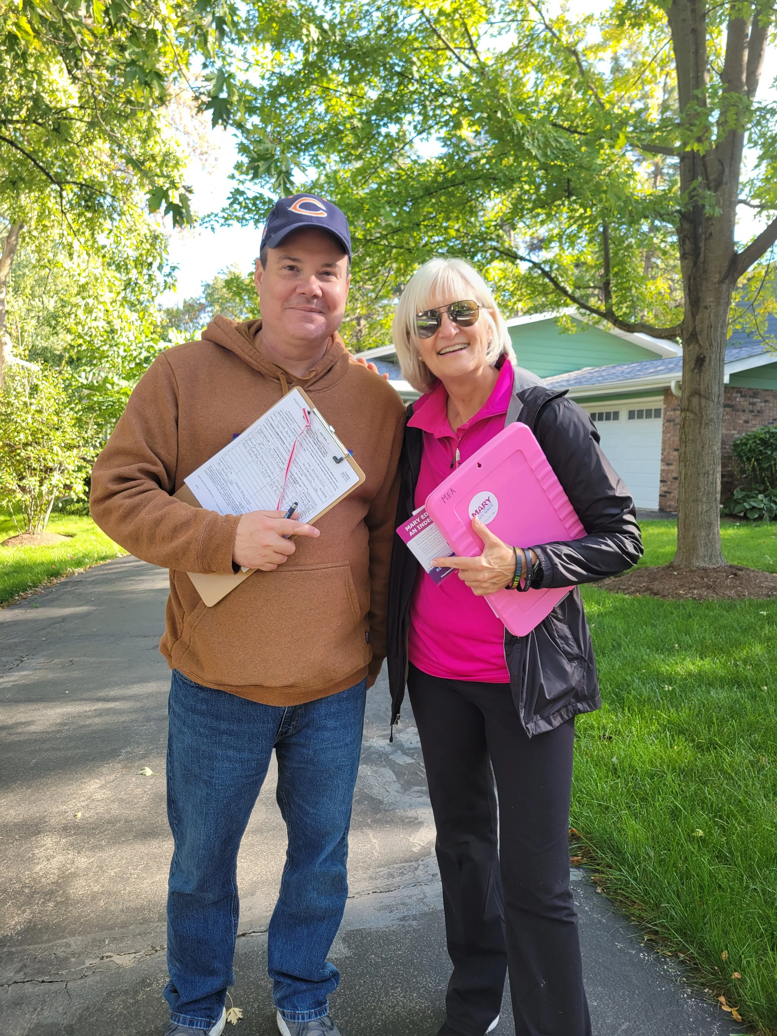 Mary Edly-Allen and Brian Clark holding clipboards and standing on a driveway as they canvass a precinct.