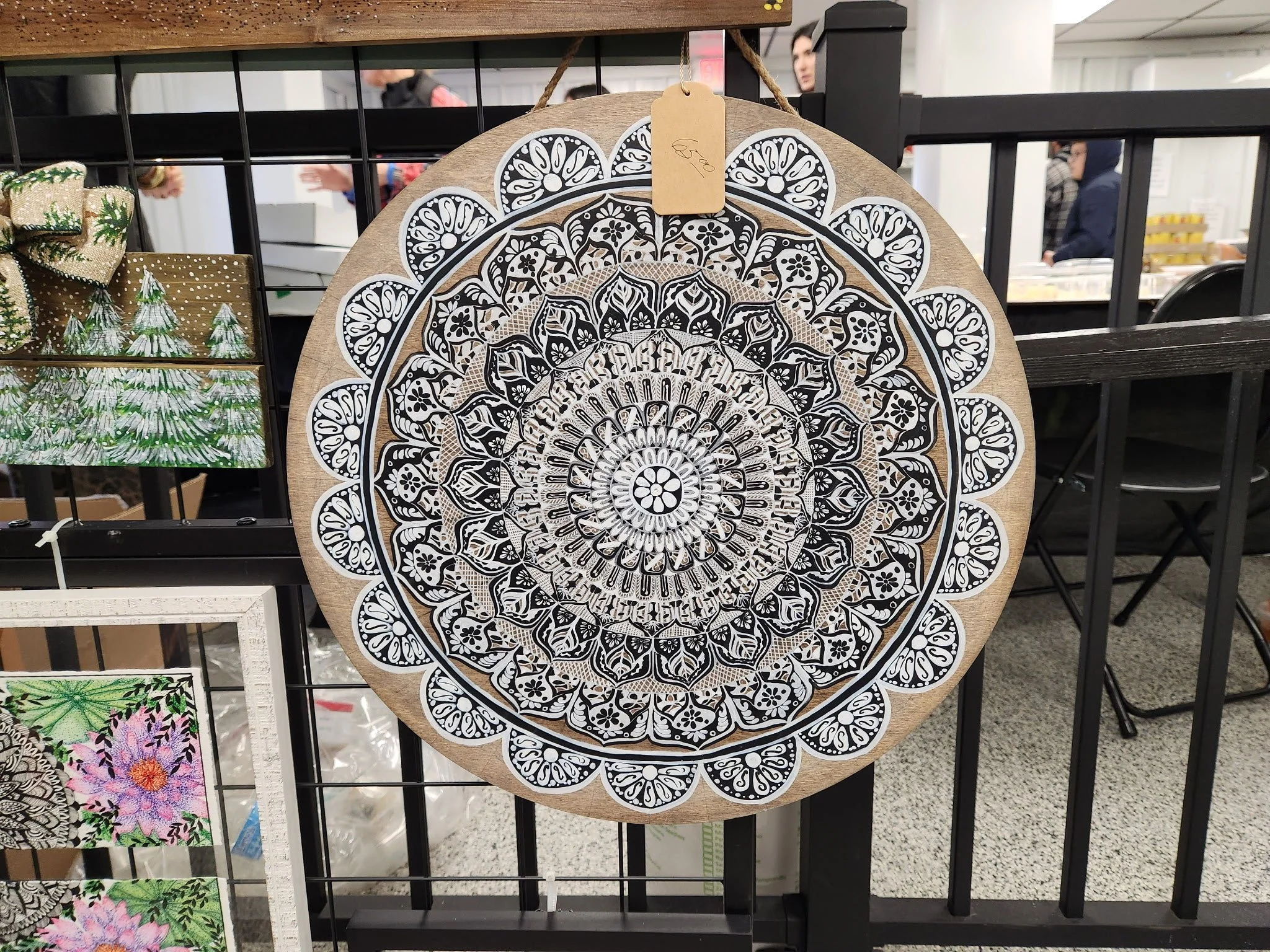 Decorative round mandala painted on wood with black and white intricate patterns, displayed at a craft market.