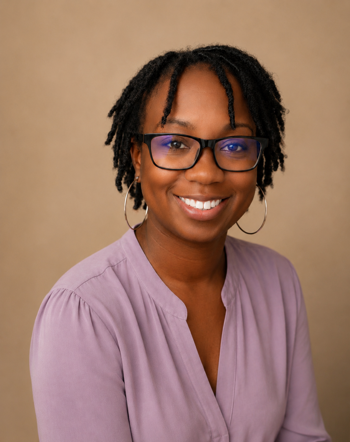 A smiling woman with glasses, hoop earrings, and short twists hairstyle, wearing a purple top, against a beige background.