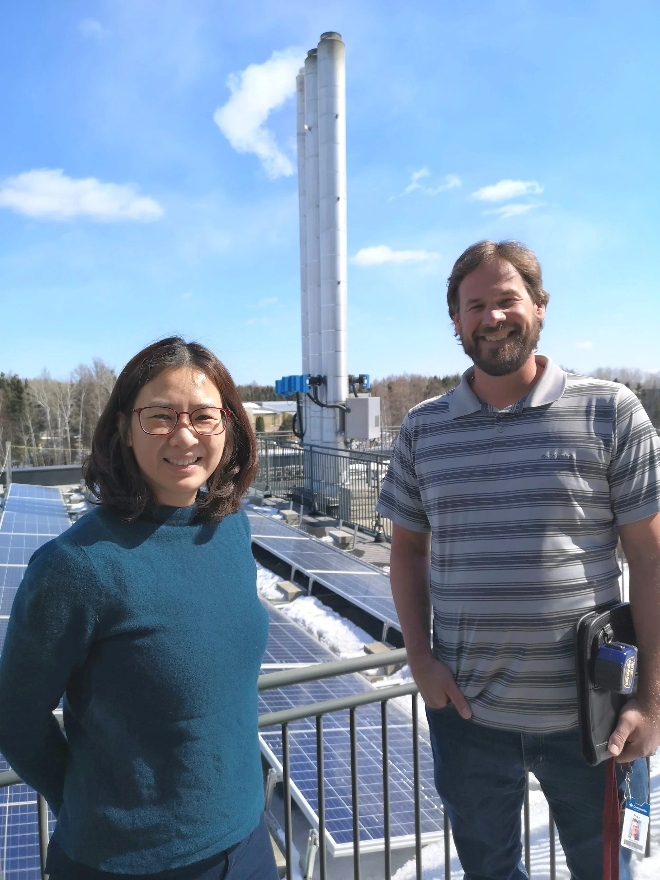 Scenic landscape with a large lake, green rolling hills, and mountains in the background under cloudy sky.