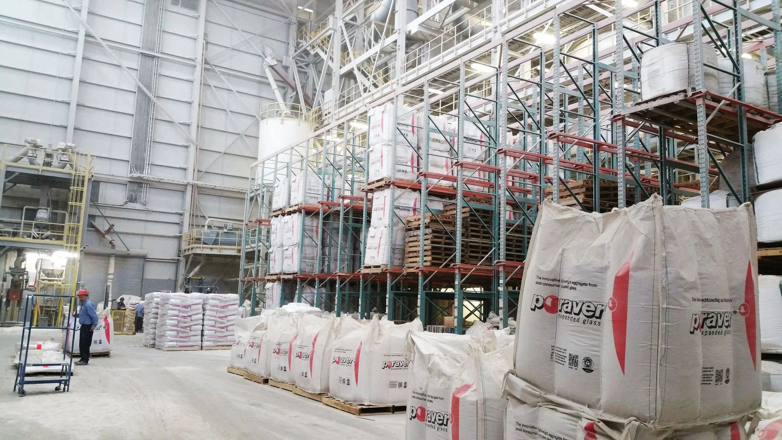 A modern building with wooden exterior walls and a large glass window, set against a mountainous landscape with dry grass and sparse trees in the foreground.