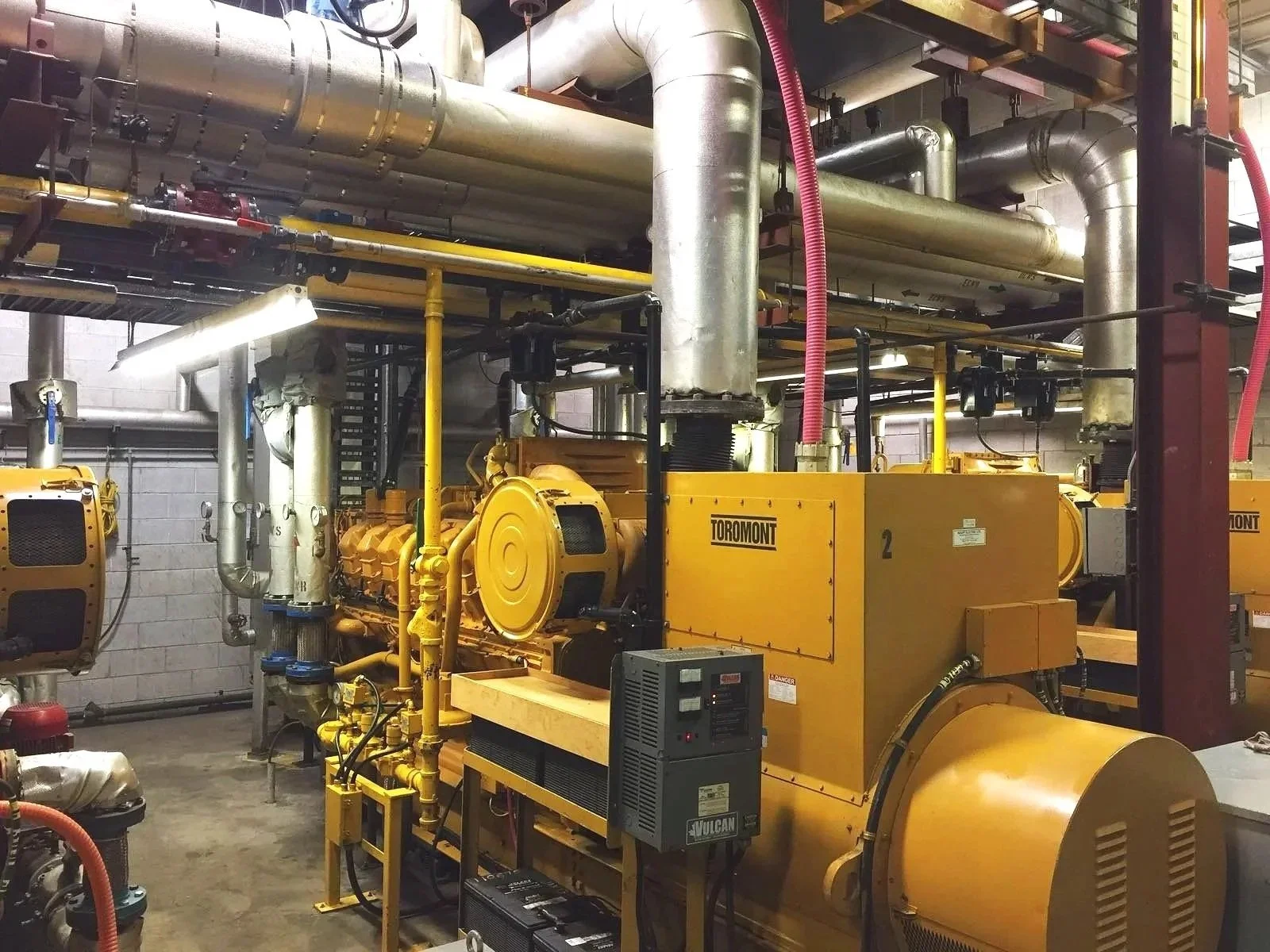 A small modern house on a grassy hillside with a mountain range in the background, featuring snow-capped peaks and cloudy skies.