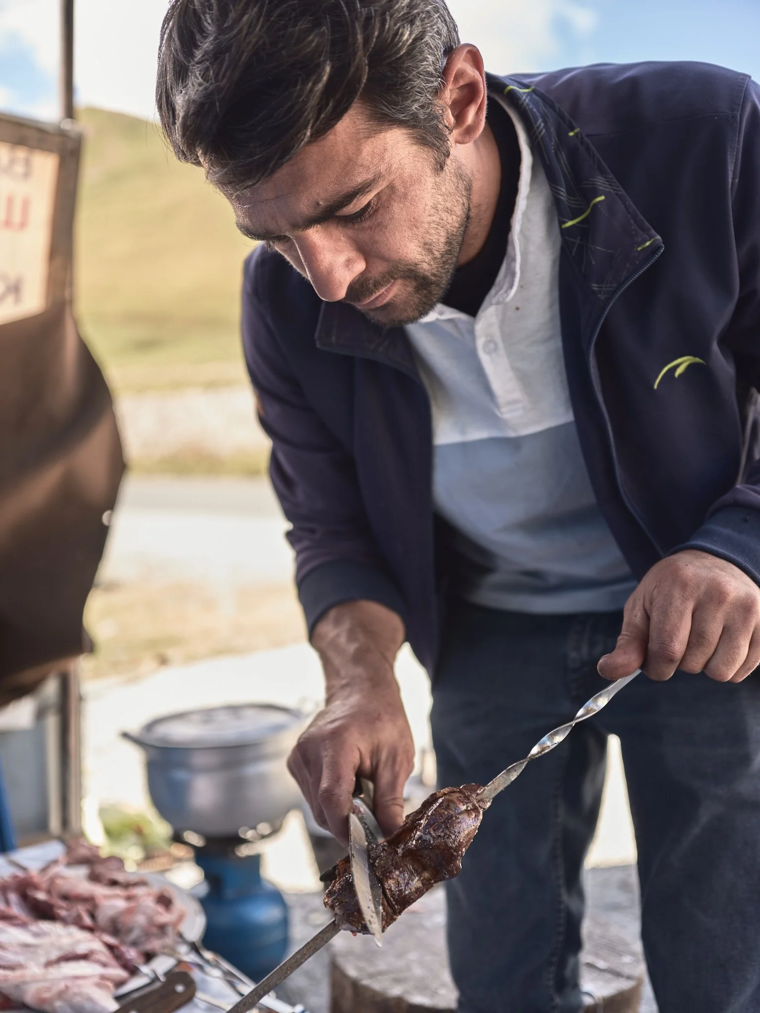 Man carving cooked meat from a rotisserie spit outdoors