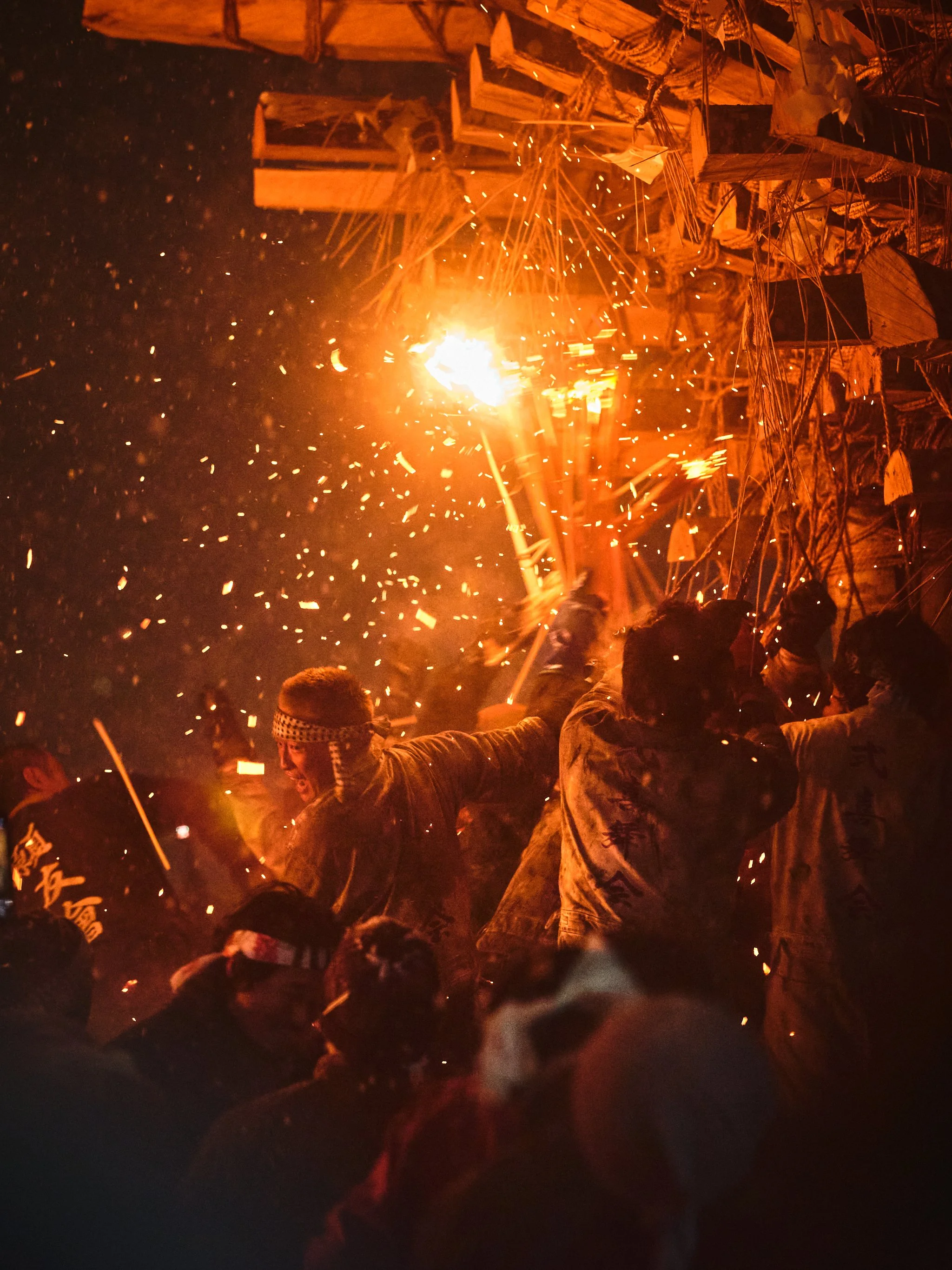 People celebrating during a festival or event at night, lighting firecrackers and fireworks, with traditional decorations and structures in the background.