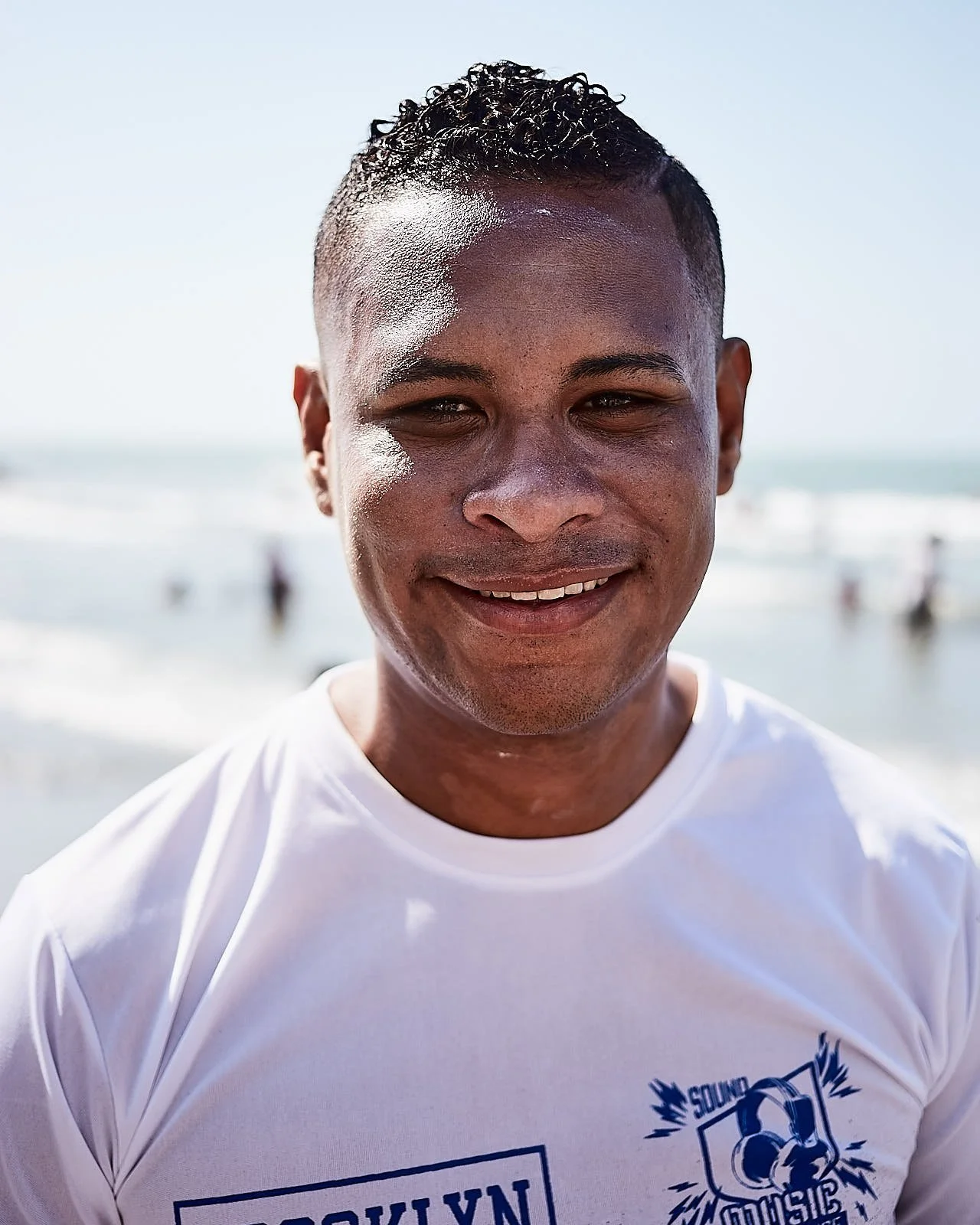 Smiling man at the beach with ocean waves in the background.