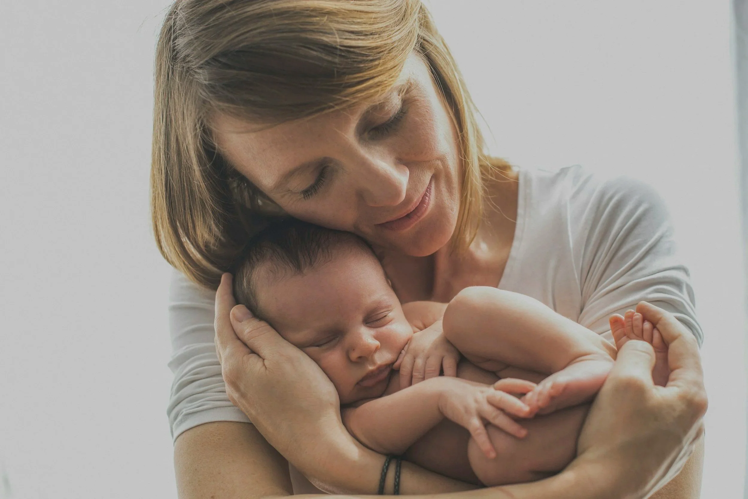 A woman lovingly holding a sleeping newborn baby close to her chest, with both appearing peaceful and content.