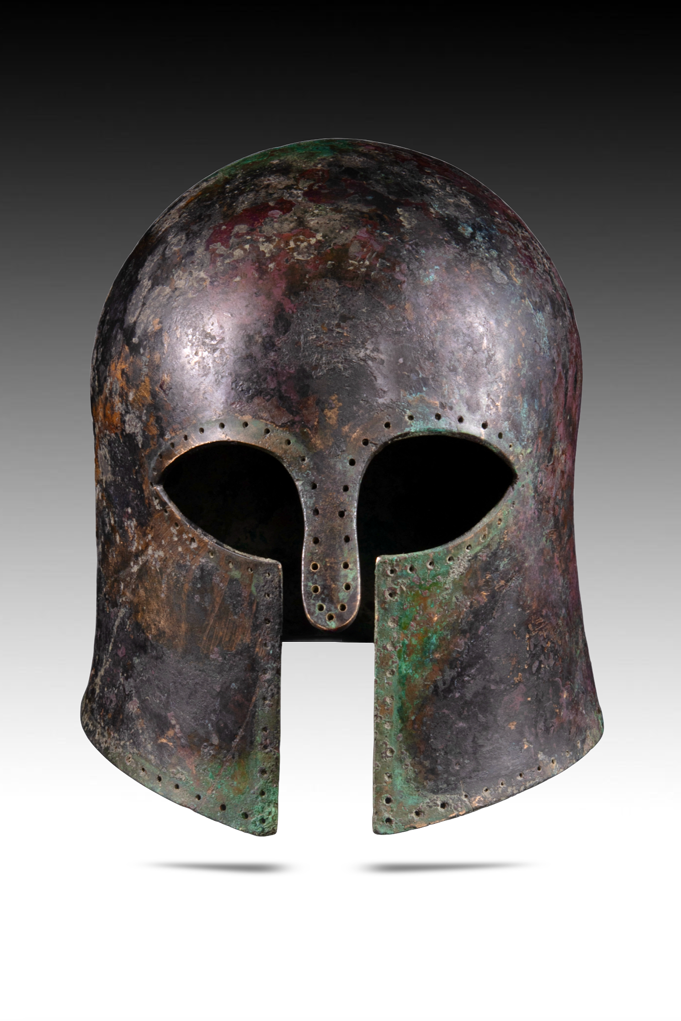 Ancient bronze mask with a split down the middle, featuring a stylized face with hollow eyes and a nose, corroded surface with green and reddish patina, on a gray background.