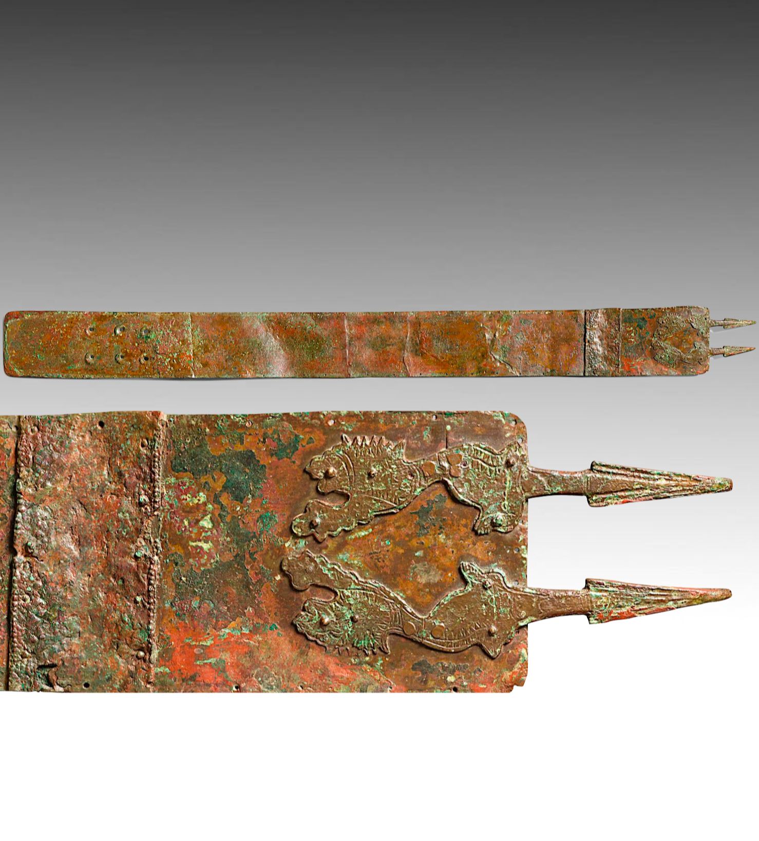 Close-up of ancient bronze sword and sheath, weathered with green and reddish corrosion, featuring a detailed dragon or horse motif on the sheath.
