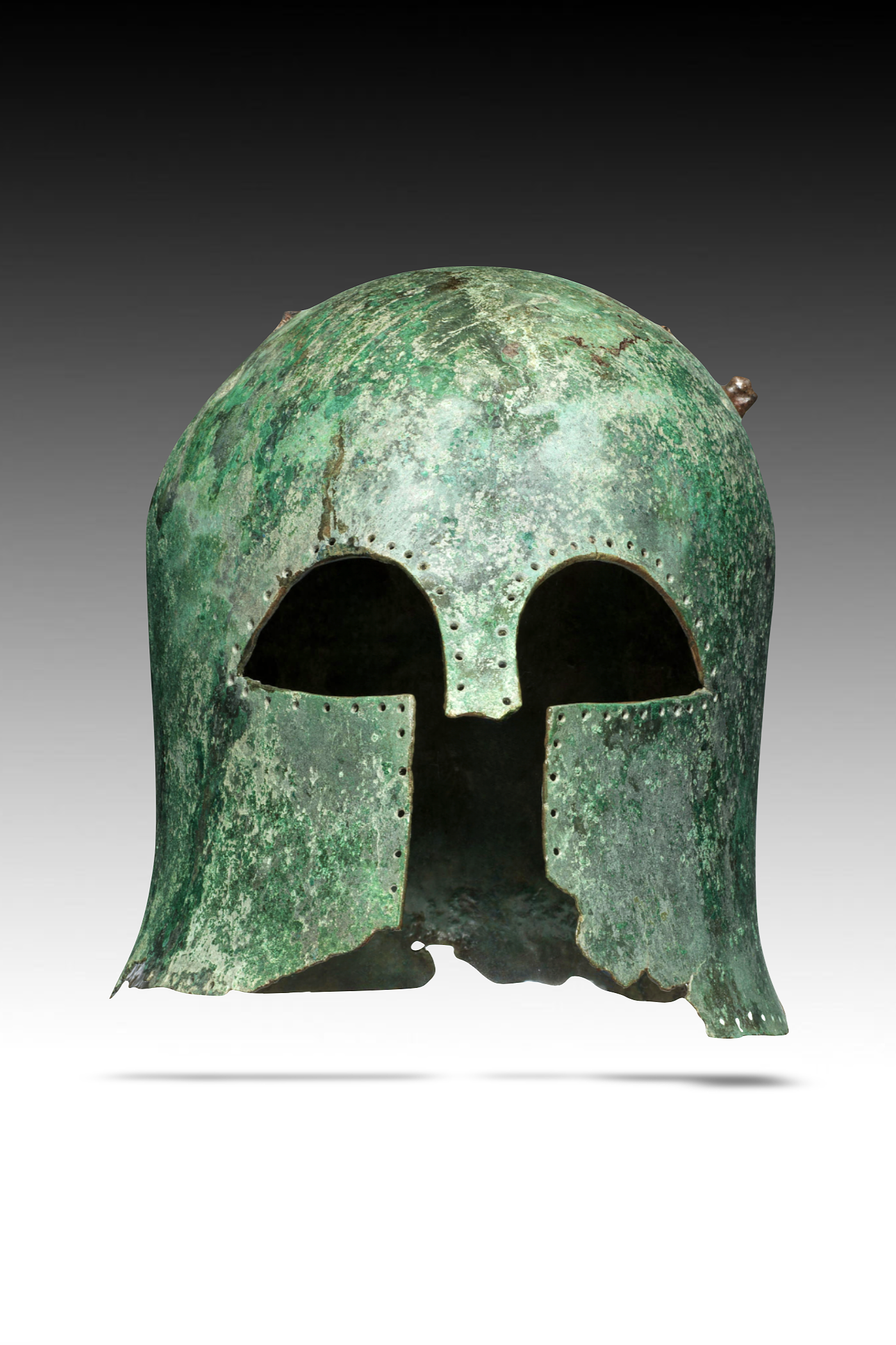 Ancient bronze helmet shaped like a human skull, with a weathered green patina and damage at the edges.