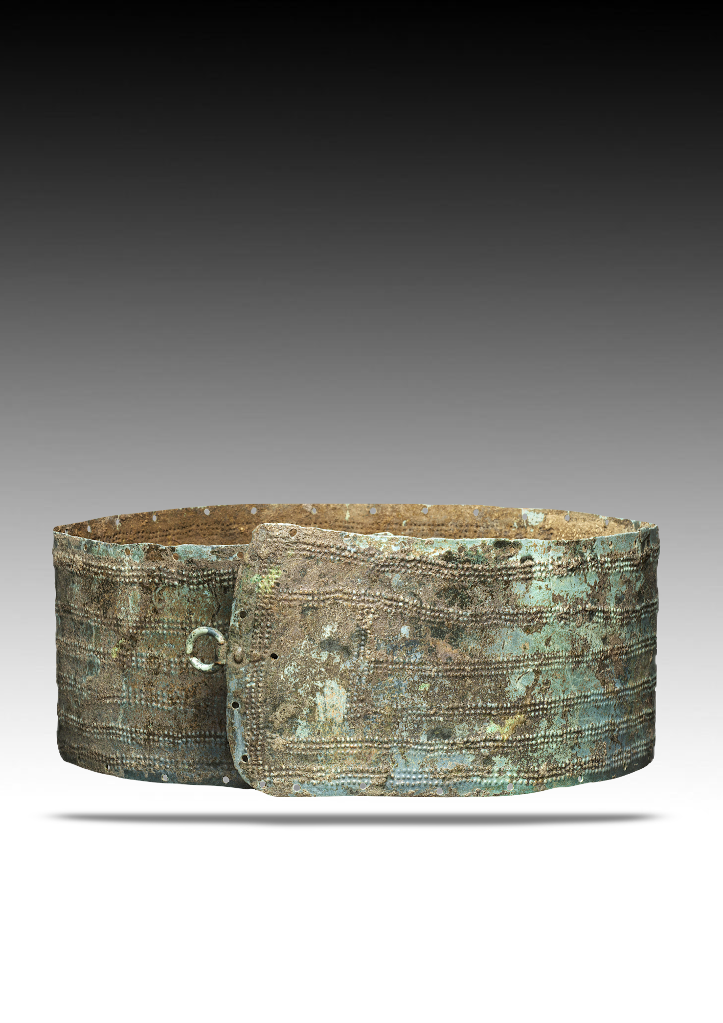 A large, round, ancient metal object with a rusted and corroded surface, featuring a series of small holes and a handle, looks like an old, weathered shield or basin.