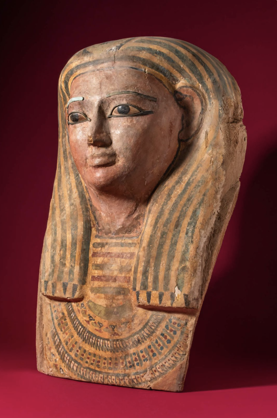Ancient Egyptian painted wooden bust of a woman with a striped headdress and decorative jewelry.
