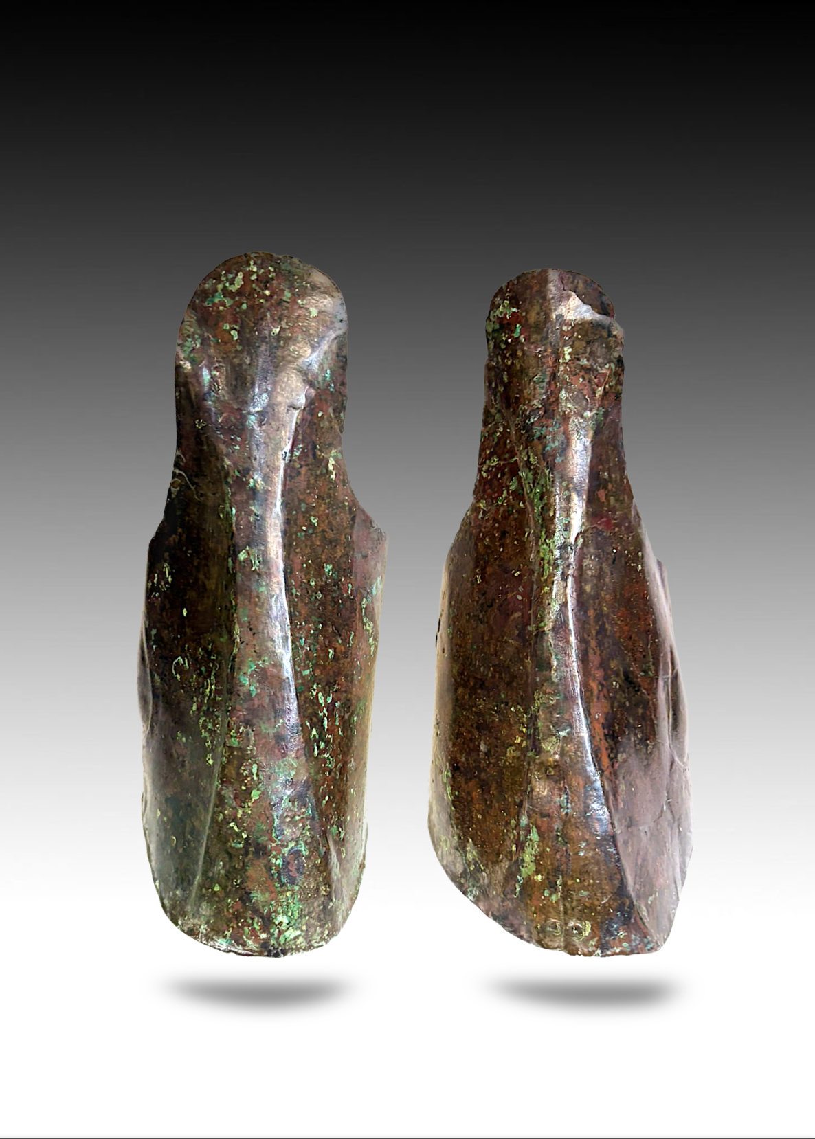 Two ancient, weathered bronze artifacts, possibly tools or sculptures, with a green patina and irregular surface textures, standing upright against a gradient background.