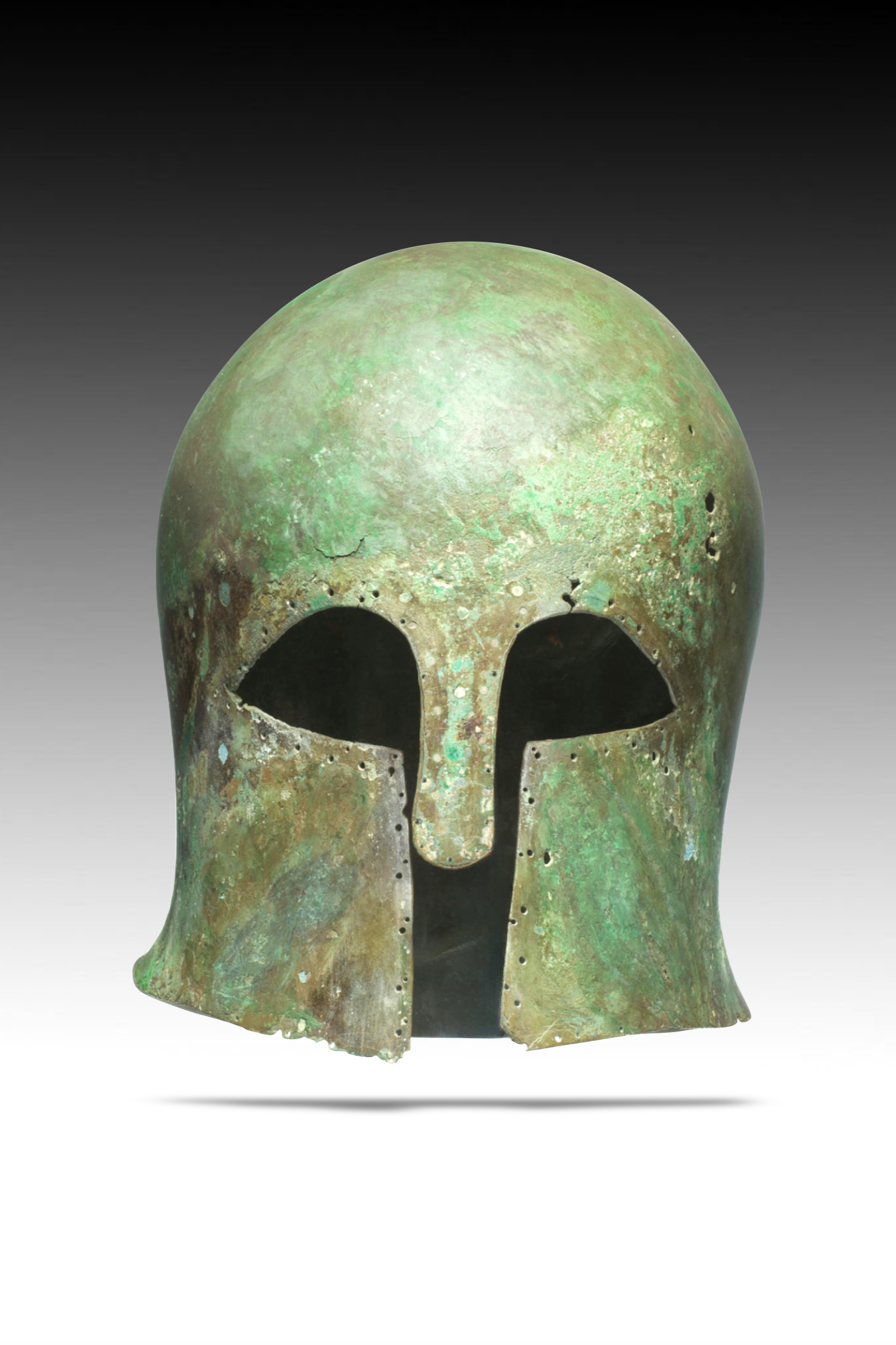 Ancient bronze helmet with a green patina, shaped like a human skull, featuring eye sockets, a nasal opening, and decorative perforations along the sides.