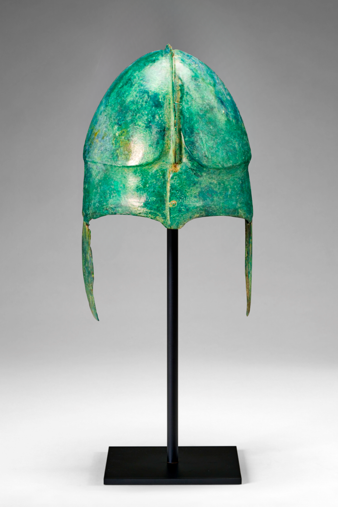 Ancient bronze helmet with a green patina on a black stand