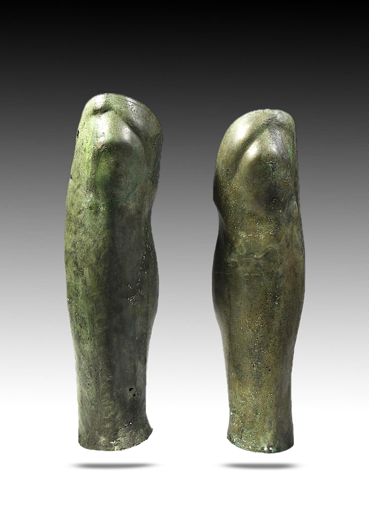 Two ancient bronze figurines resembling abstracted human torsos, standing upright with rounded shoulders, with a greenish patina and a textured surface.