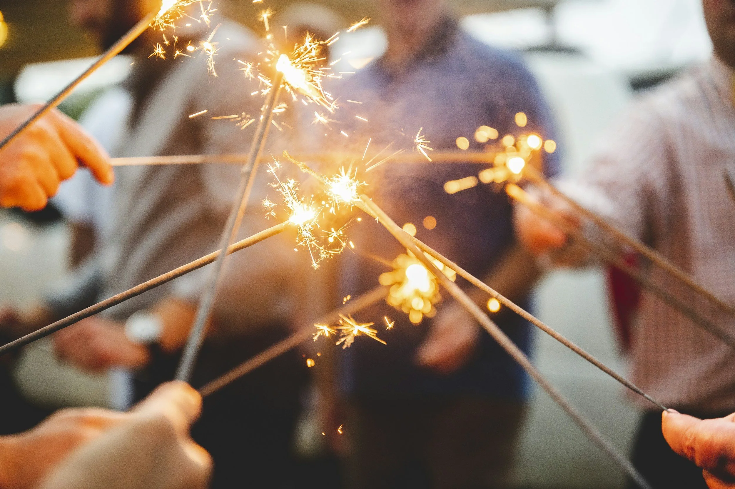 People holding sparklers in a circle during a celebration, with bright sparks and blurred background.